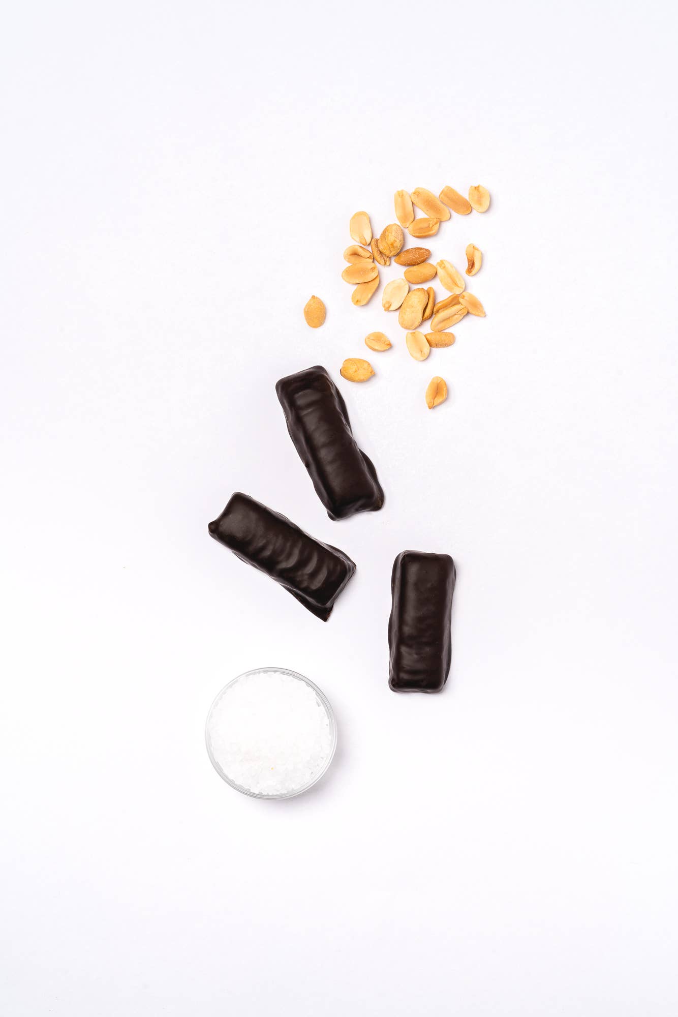 A group of chocolate date bars with peanuts, coated in dark chocolate, on a white surface. Made with premium dates and roasted peanuts, sweetened with coconut sugar. Perfect for Fall snacking.
