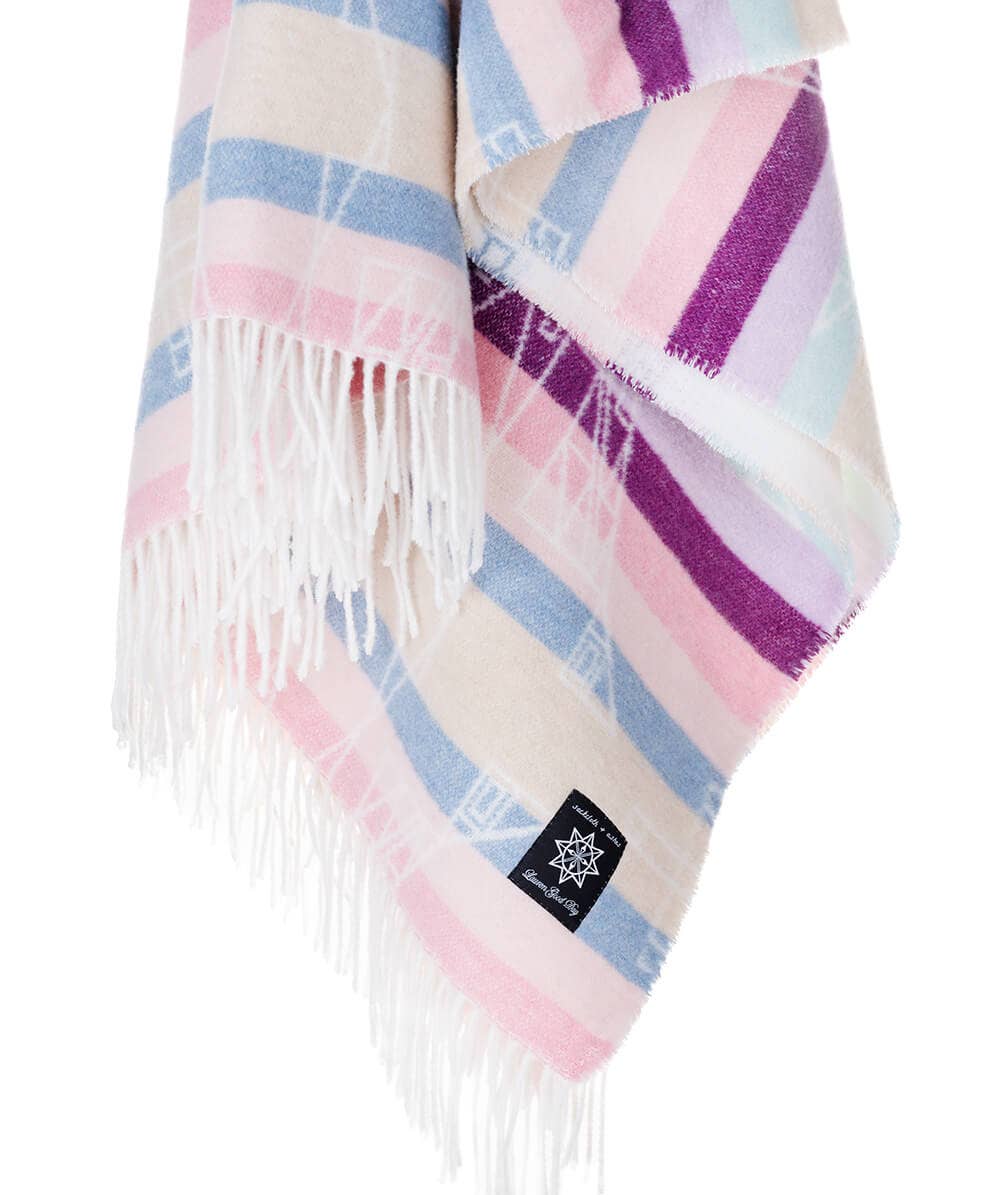 A blanket with fringes, featuring Lauren Good Day's Seasons design Hunaaneeká (Spring). Made from recycled materials in a sustainable process. Size: 72”l x 60”w. Textile art by an Indigenous fashion designer.