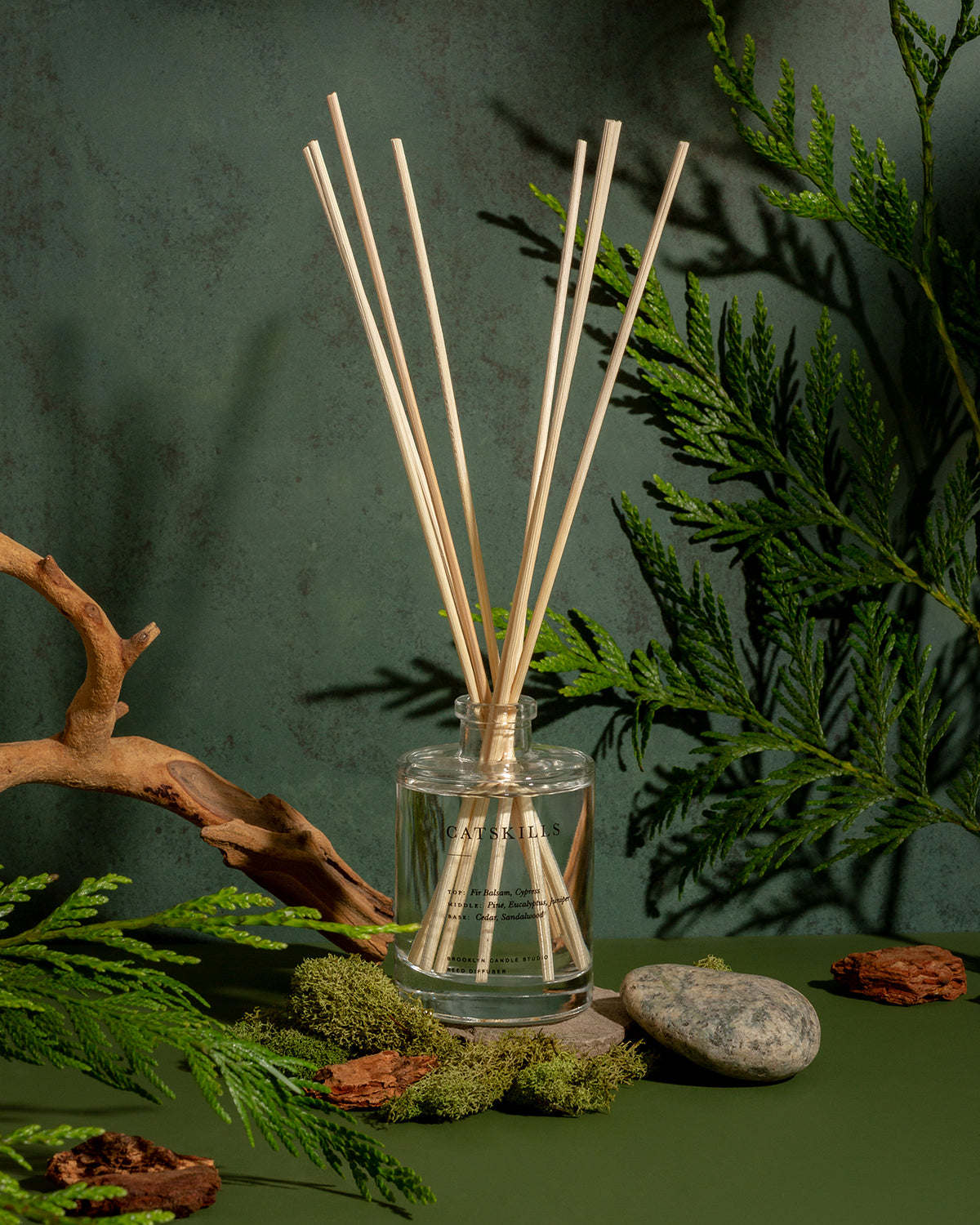 A glass bottle with wooden sticks, embodying the Catskills Reed Diffuser from the Escapist Collection by Brooklyn Candle Studio. Evoking a forest hike with cedar, cypress, and juniper scents.