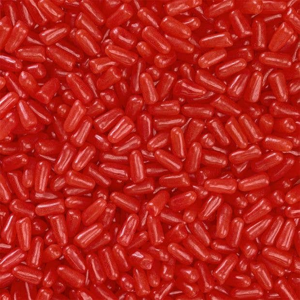 A close-up image of many tiny, shiny red candy pieces, each roughly cylindrical in shape. The candies are densely packed, covering the entire frame. These Hot Tamales 5oz Theater Box, Fierce Cinnamon Candy 12ct from Grandpa Joe's Candy Shop add a vibrant pop of color and a hint of spice.