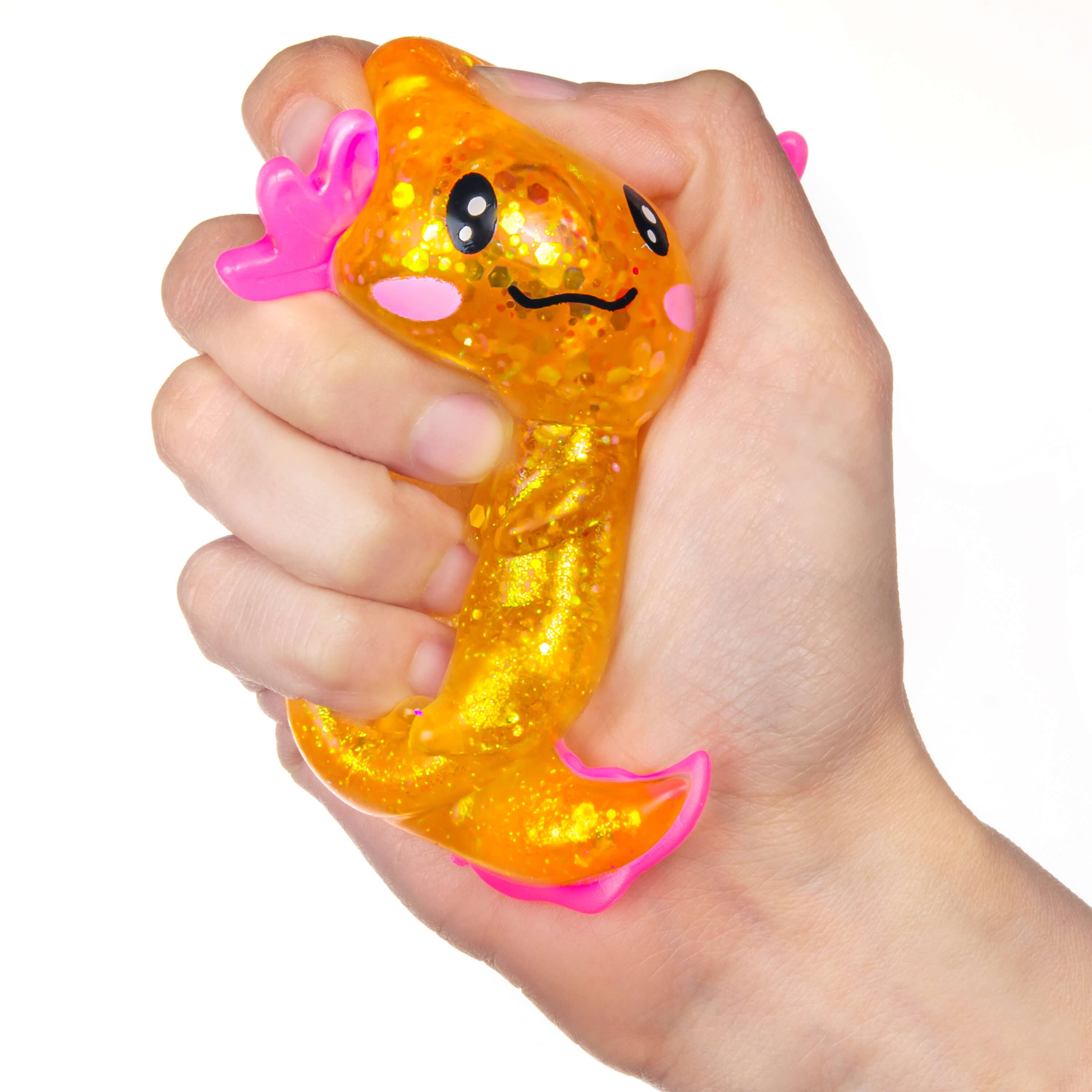 A hand holds a yellow squishy toy, Gummy Axolotl Pets, in glittery colors. Sensory stress relief in 12 pieces per case.