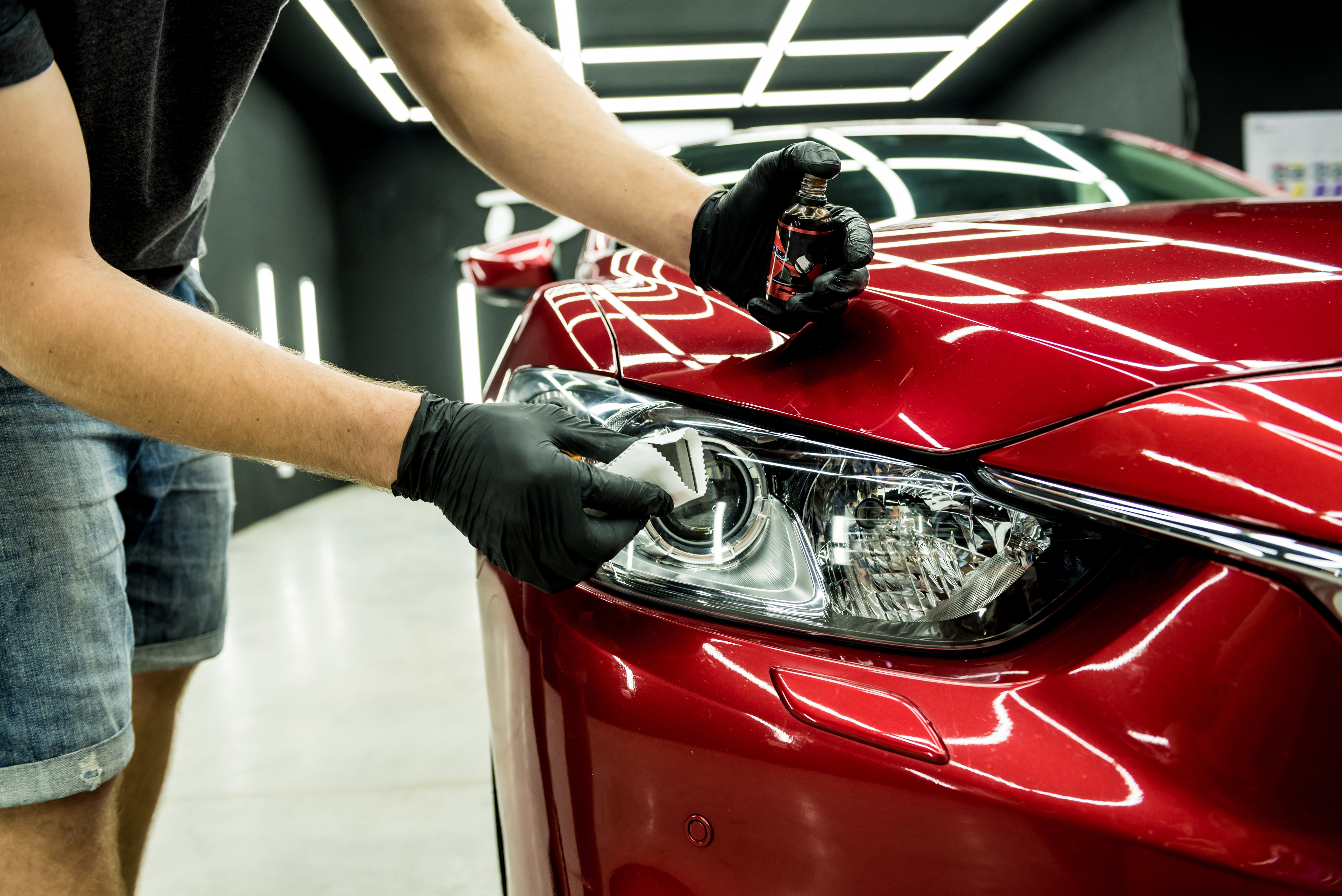 Person polishing a red car's headlight for Gloss's Headlight Restoration service, ensuring crystal-clear lenses for dancing in radiant light.