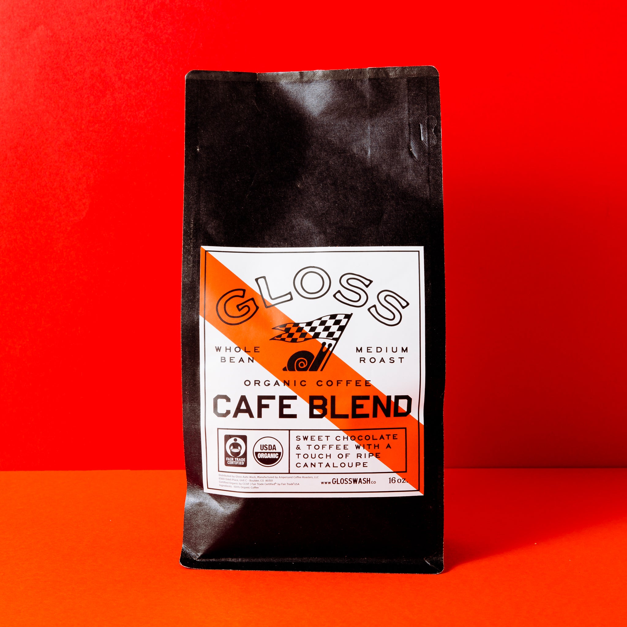 A black bag featuring a white label and orange logo, close-up of the Gloss Cafe Blend Coffee 16oz Bag branding.