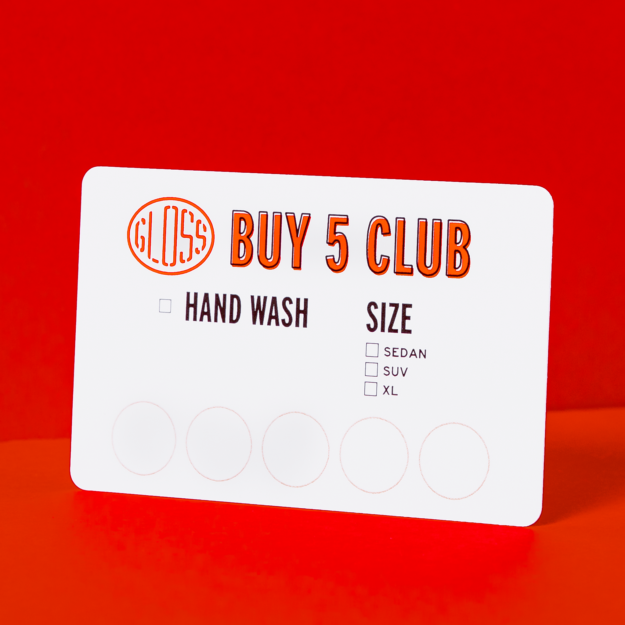 A white card displaying Buy Five Card with orange text and numbers, alongside circles, on a red surface. Join our Buy 5 Club for 10% off hand washes, car washes, or express exterior washes.