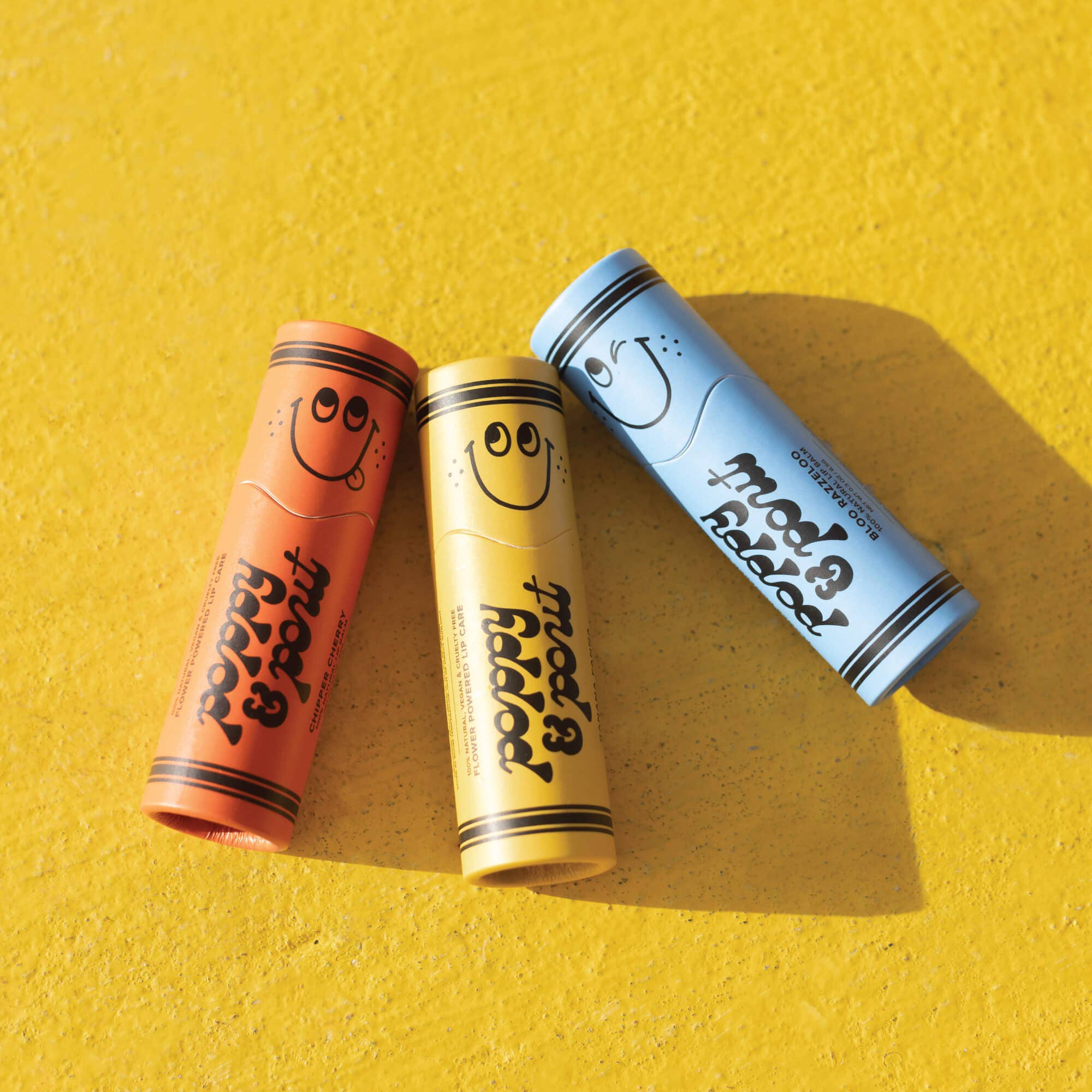 A close-up of Bloo Razzeloo lip balm tube from Lil' Poppies collection, featuring a blue and yellow design with black text.