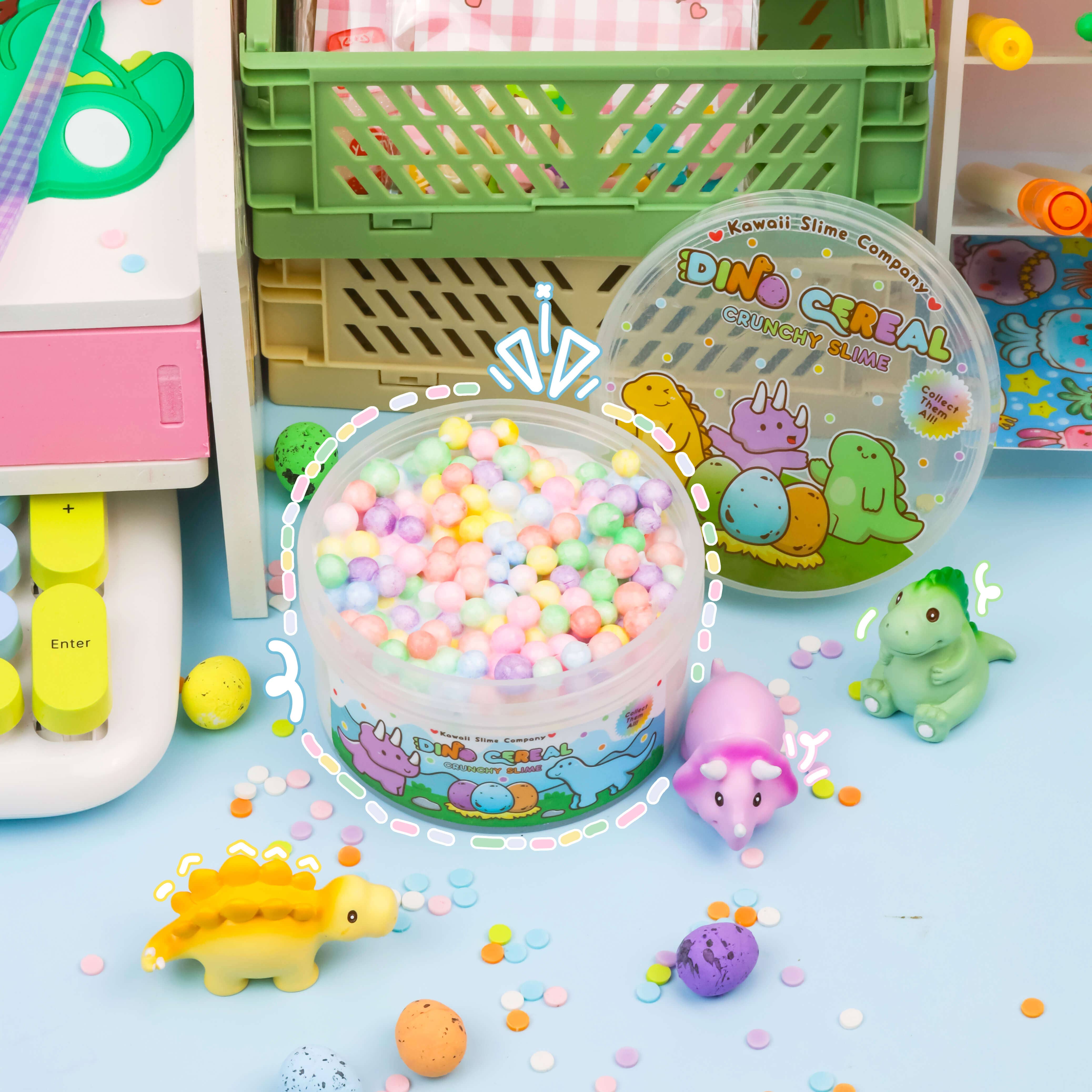 A plastic container filled with colorful balls, dinosaur toys, and play dough. Dino Cereal Crunchy Slime (4pcs/case) includes confetti sprinkles, dino eggs, and collectible dinosaur miniatures.