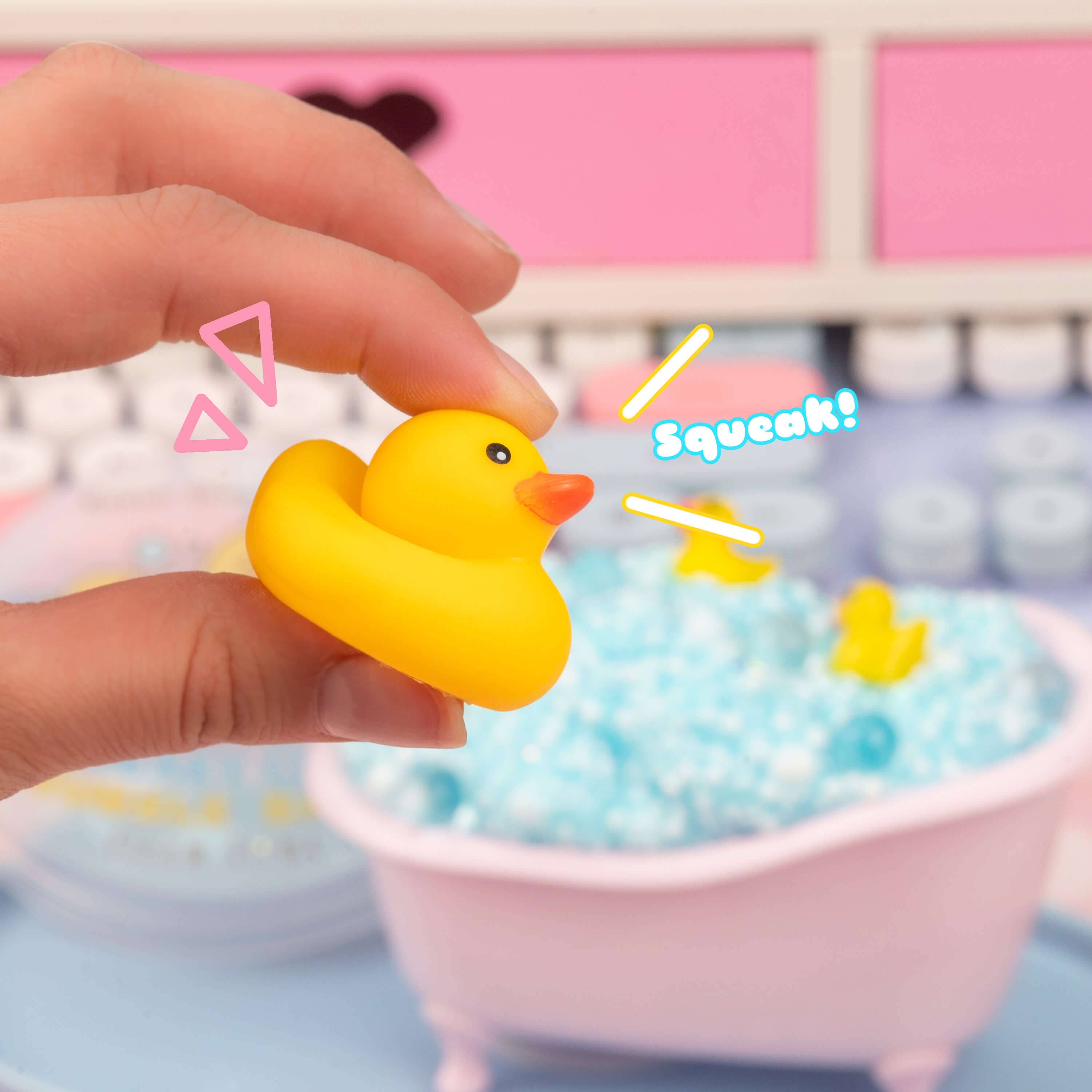 A hand holding a yellow rubber duck, part of Squeaky Clean Bubble Bath Floam Slime. Includes foam beads, glitter, and a floral scent. Cute squeaky duck toy included.