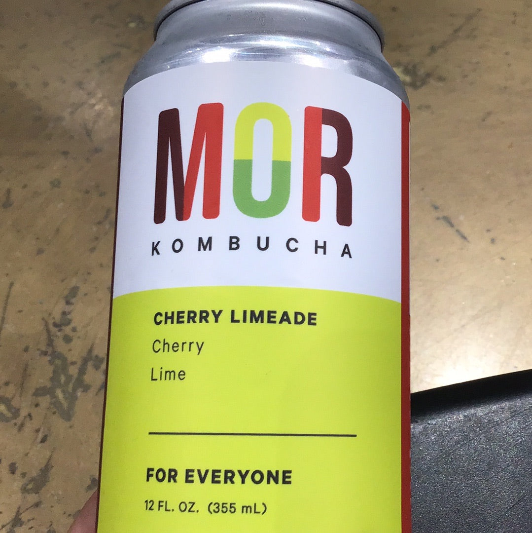 A close-up of Mor Kombucha Cherry Limeade beverage can with a label featuring a red letter b on a white surface.