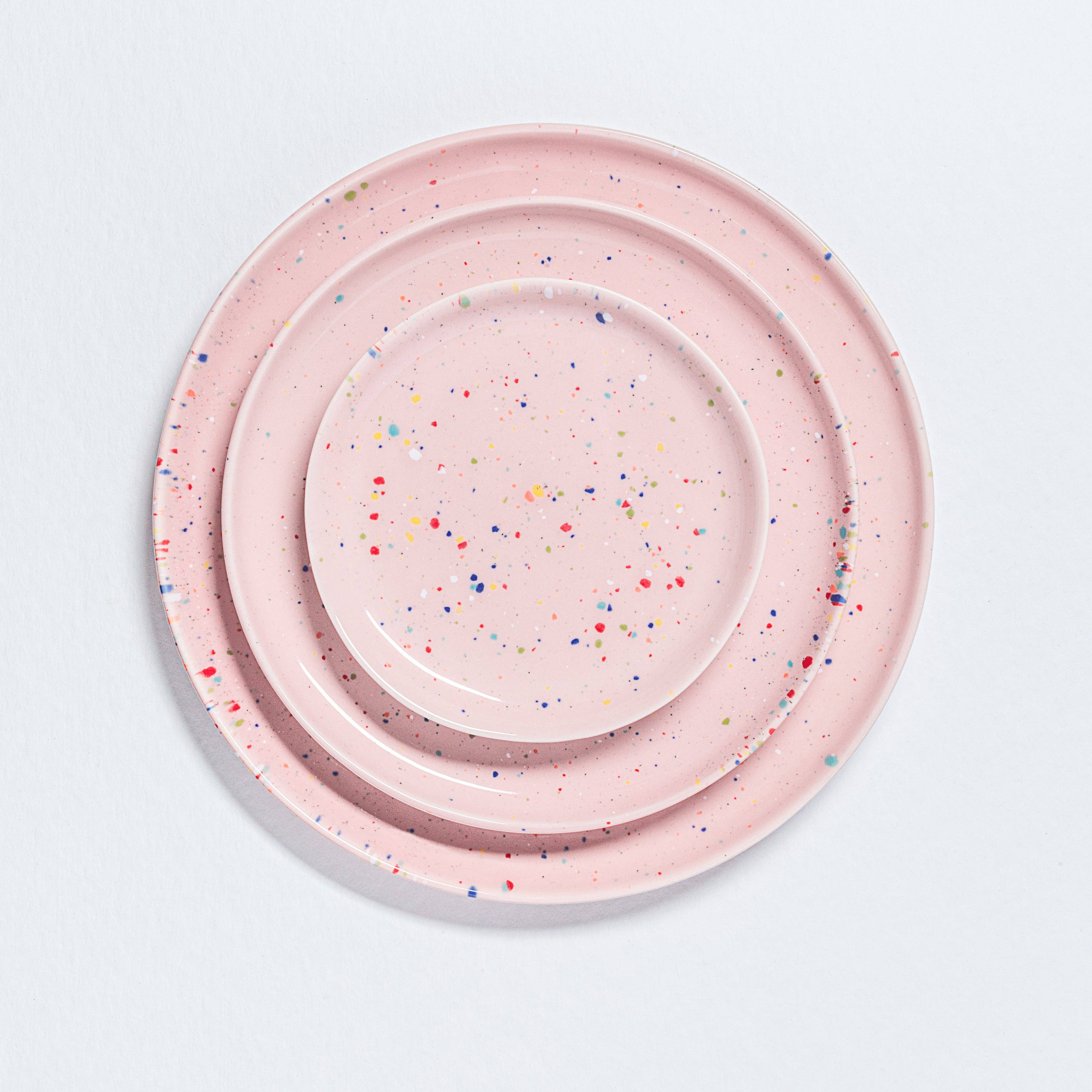 A stack of pink plates, including a plate with a speckled pattern, showcasing the New Party Bread Plate 17cm Pink. Crafted uniquely, dishwasher and microwave safe, part of the vibrant Party collection.