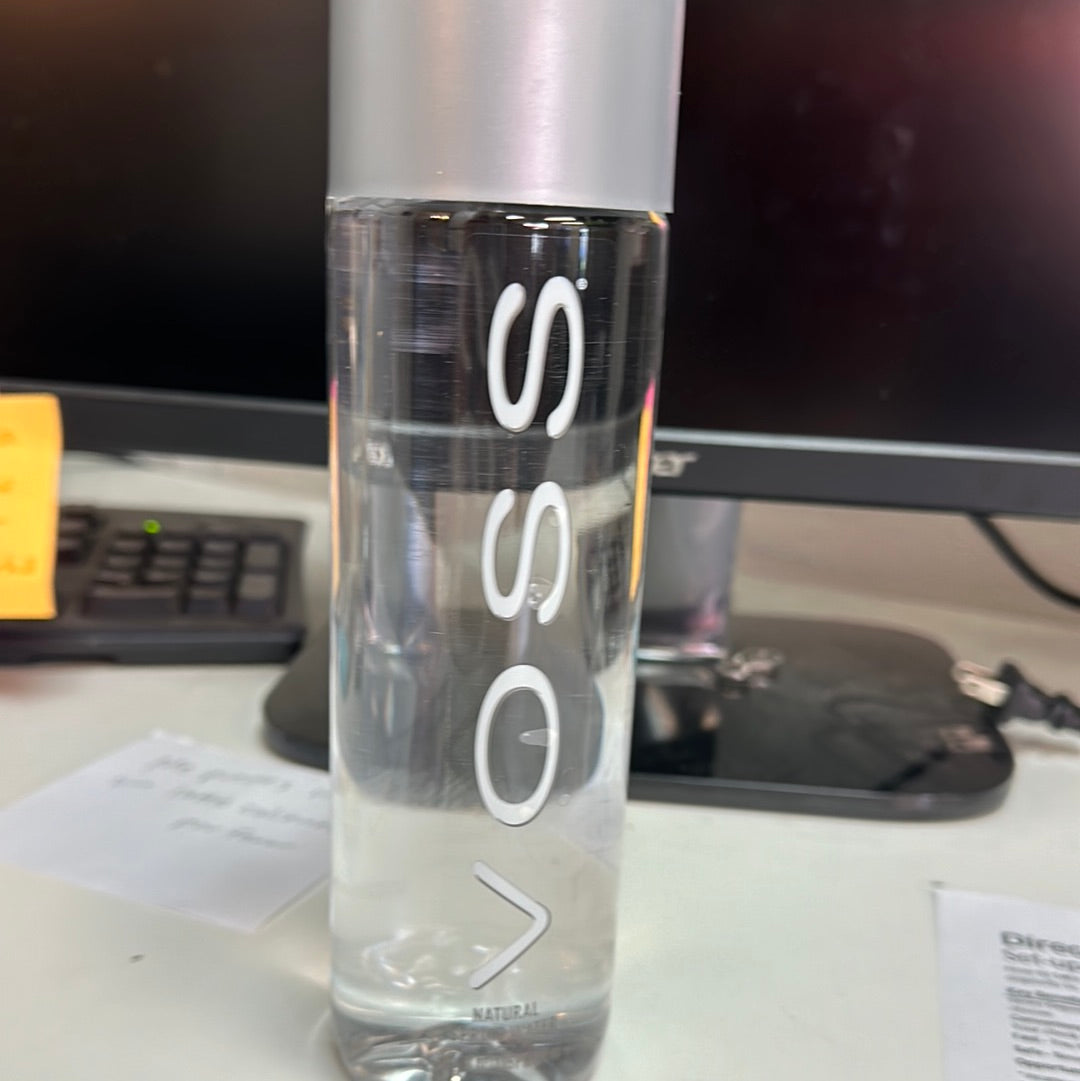 A close-up of Voss water 500ml bottle on a desk with a glass and keyboard in the background, emphasizing the product's sleek design.