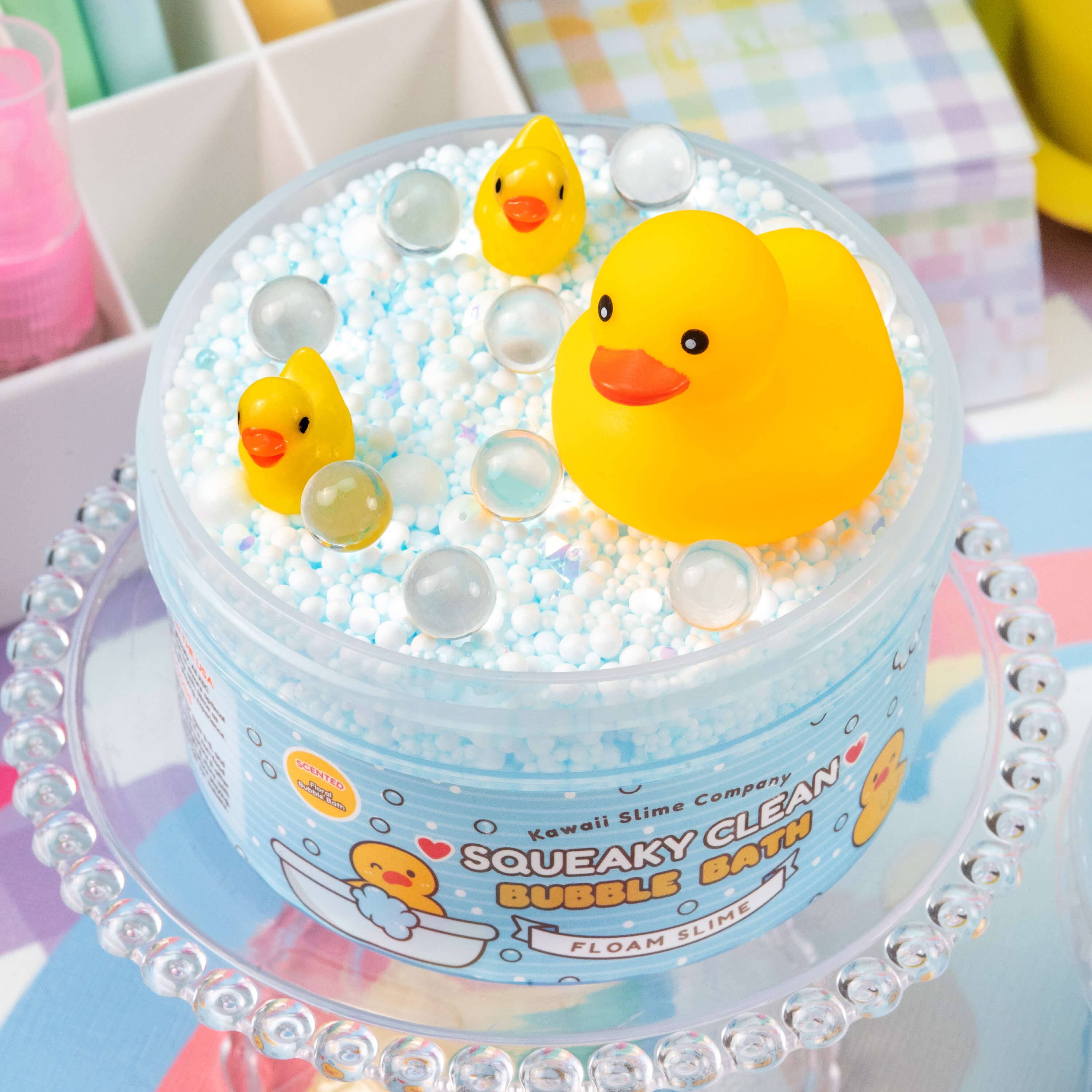 A container of Squeaky Clean Bubble Bath Floam Slime with rubber ducks, foam beads, glitter, and iridescent baubles. Floral bubble bath scented. Cute squeaky duck toy included.