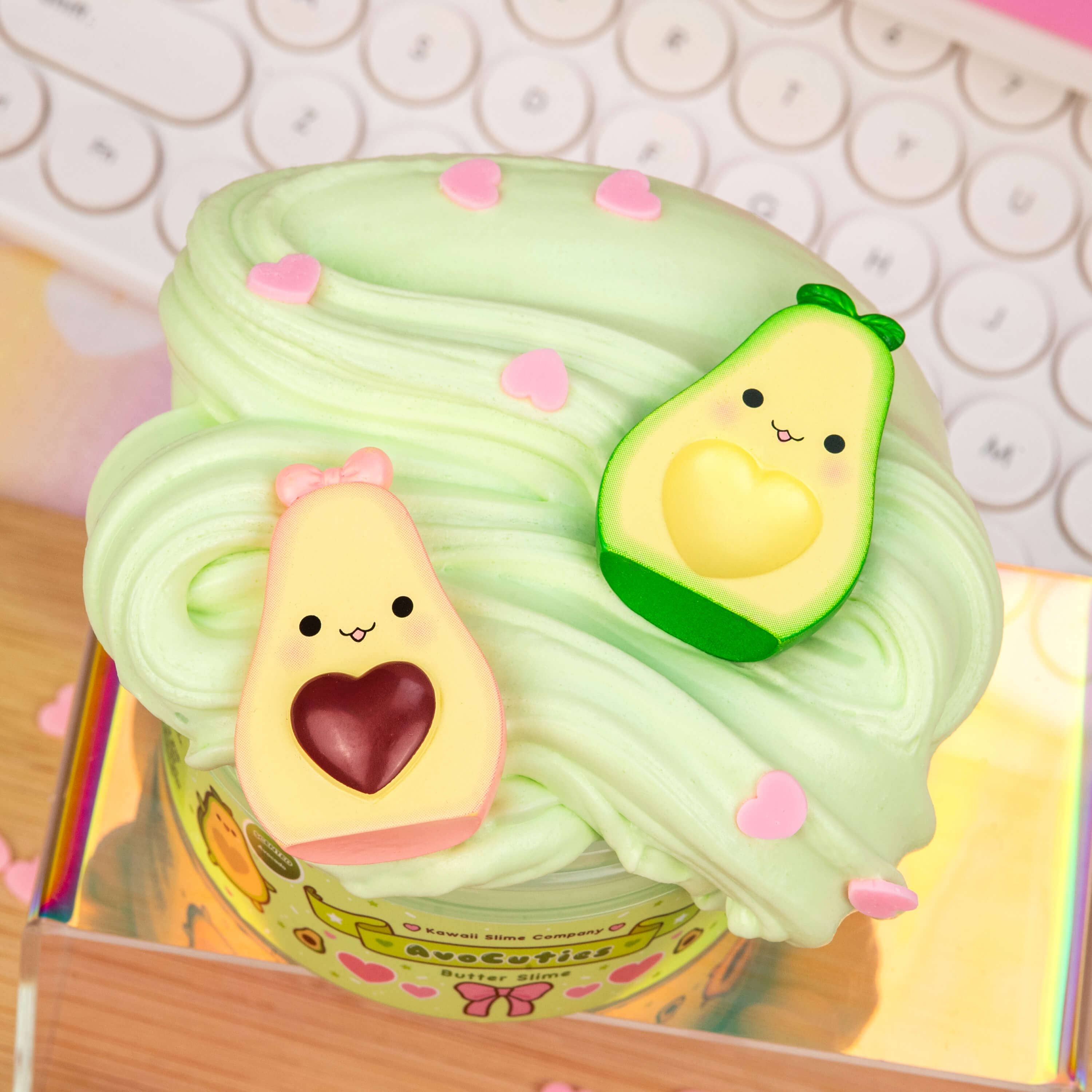 AvoCuties Butter Slime (4pcs/case) featuring a cupcake with frosting and a toy avocado on top, accompanied by heart-shaped candies and a toy avocado with a face.