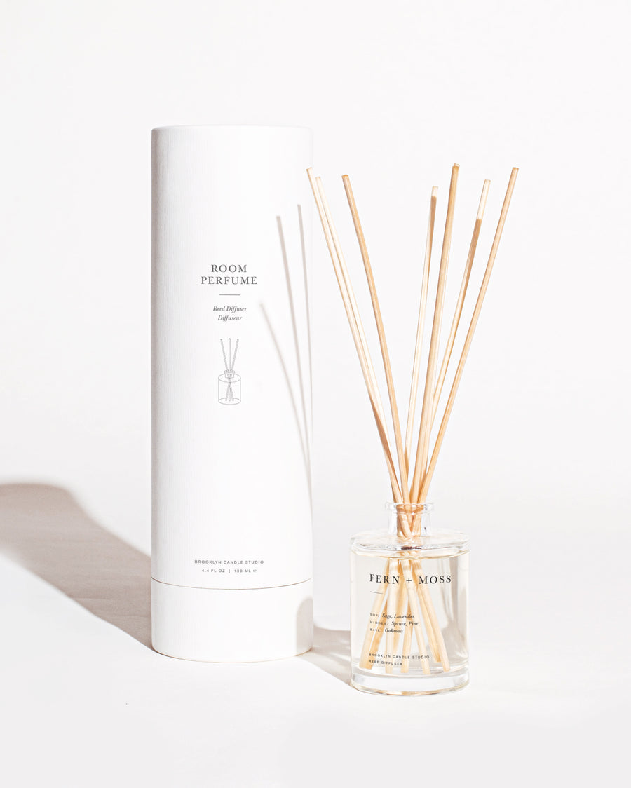 A close-up of Fern + Moss Reed Diffuser with sticks in a glass bottle, capturing a nature-inspired scent blend of sage, lavender, spruce, and pine.