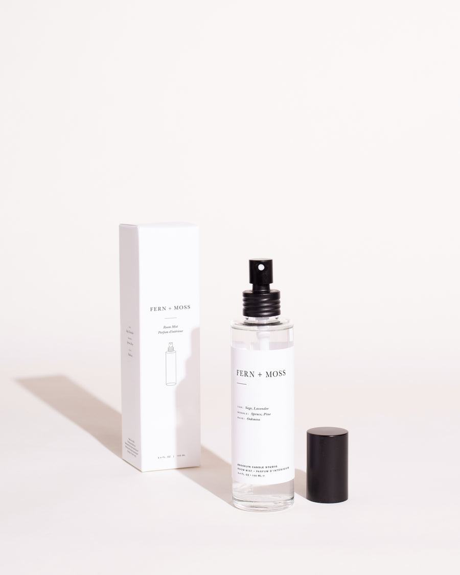 A white bottle of Fern + Moss Room Mist with black text, next to a white box featuring a spray image. Cylinder and tube elements visible.