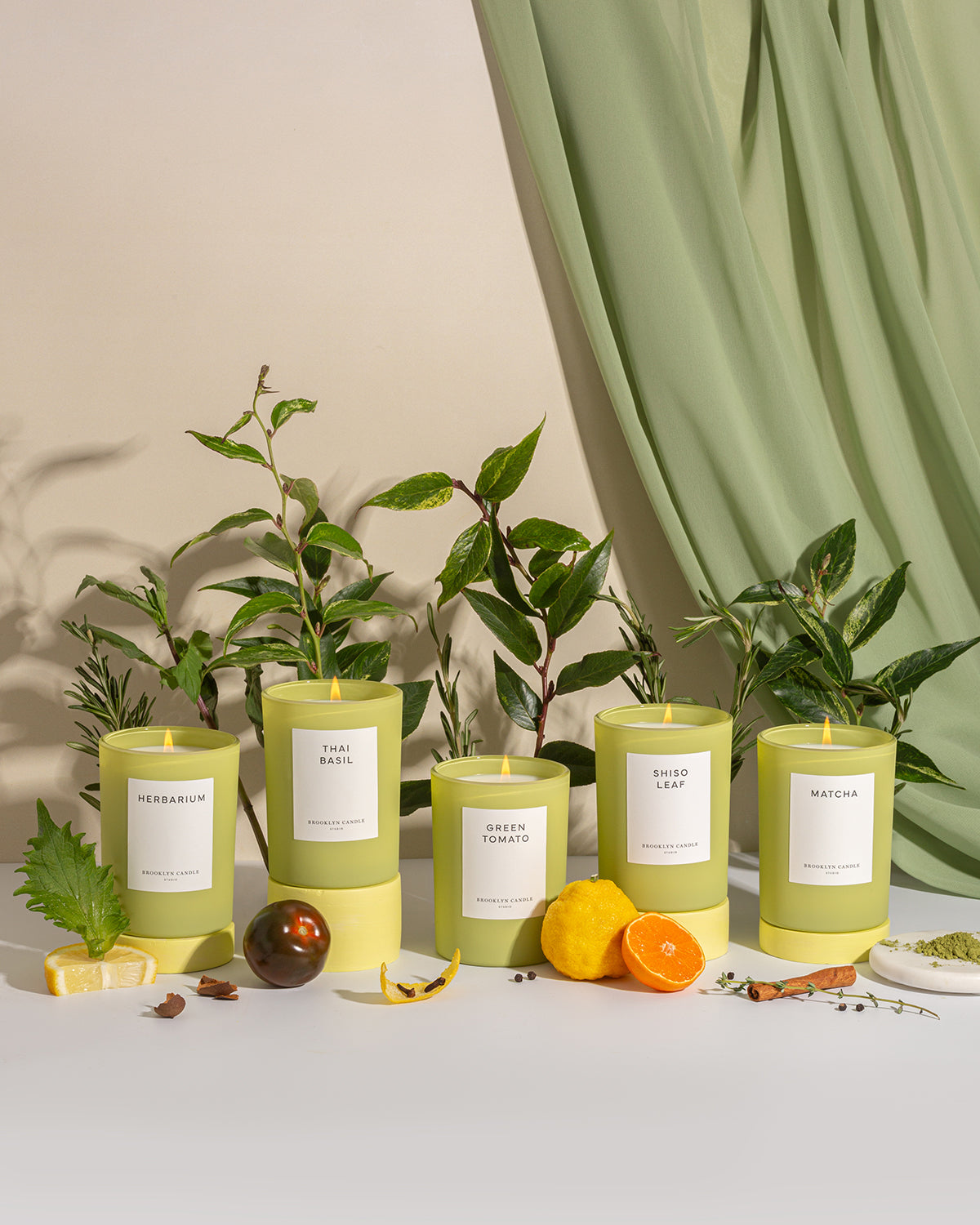 A close-up of a Thai Basil Candle in a matte chartreuse green vessel, capturing the herb's grassy, peppery essence with notes of lemon, orange, and wild mint.