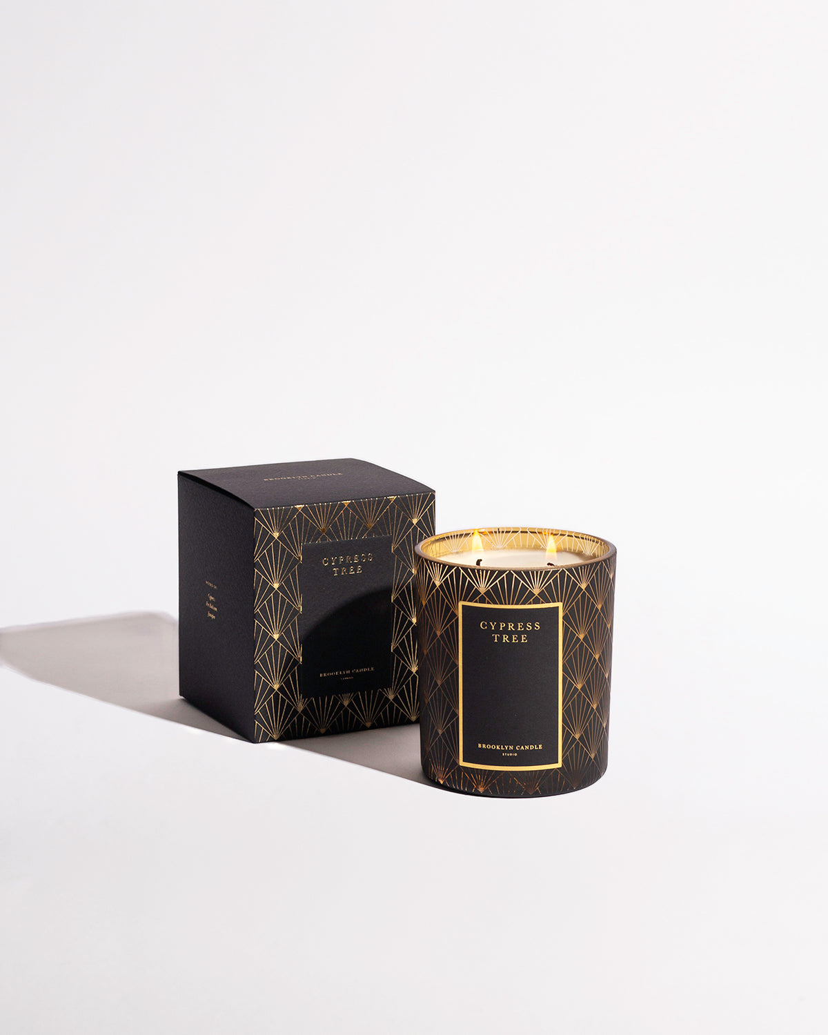 A black and gold candle in a box, embodying the essence of the Cypress Black Tie Holiday Candle. Featuring intricate gold designs on a sleek black box.