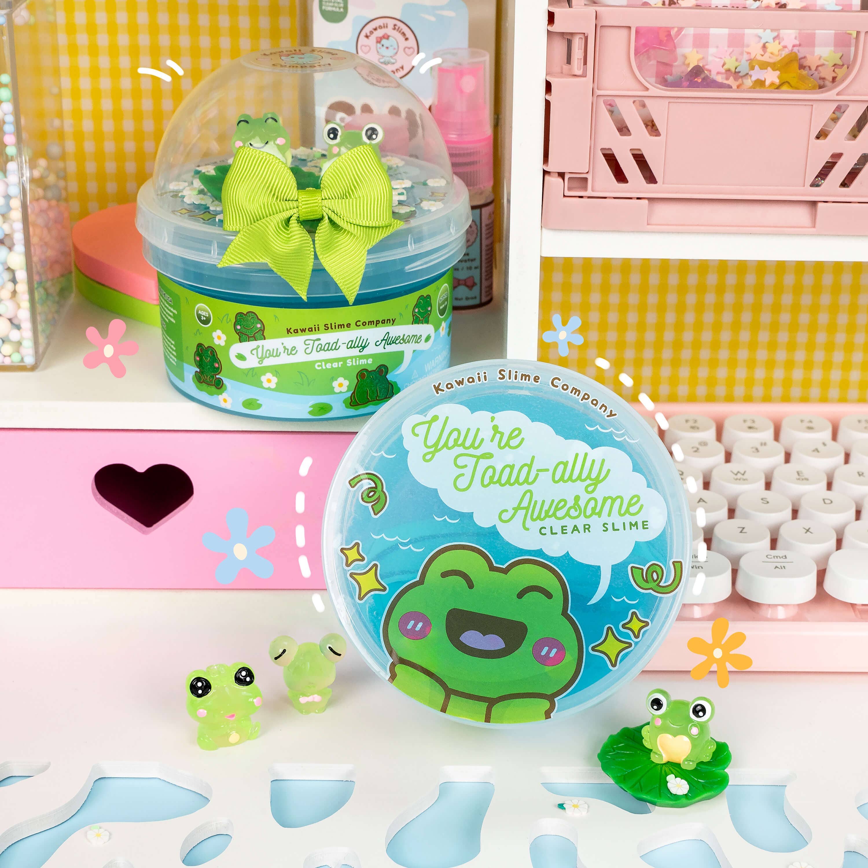 A shelf with toys, including a round blue container with a cartoon frog, a plastic container with a green bow, and a green frog toy with black eyes, representing the You're Toad-ally Awesome Clear Slime product.