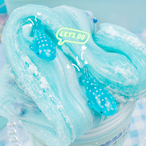 A blue slime with shark fimo slices, whale shark charms, and white meringue swirls, scented like blue raspberry candy and marshmallow cream.
