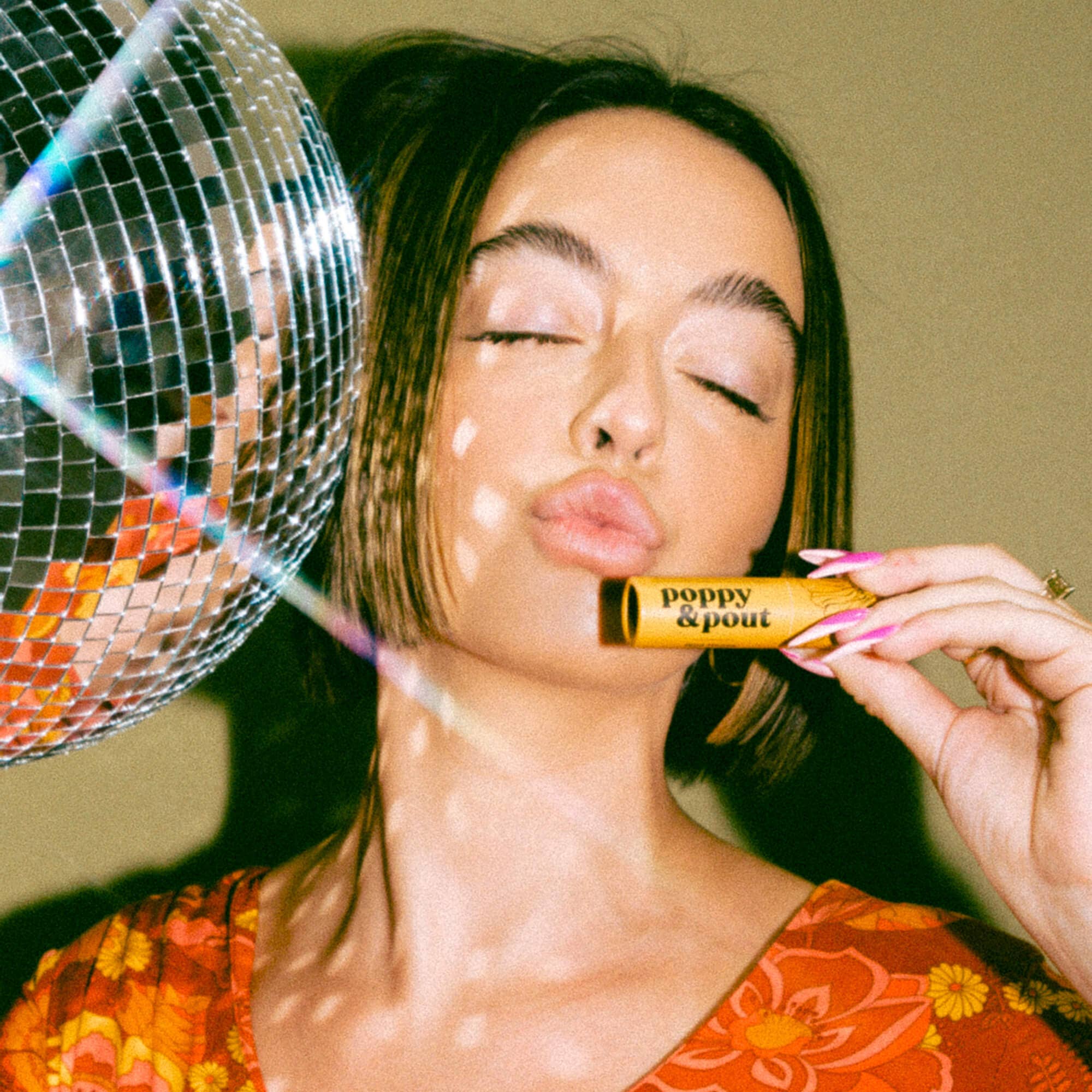 A woman holding a stick and a disco ball, emphasizing Wild Honey Lip Balm by Poppy & Pout. Hand-poured in eco-friendly tubes, 100% natural ingredients.