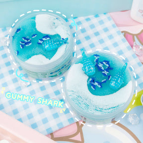 A blue and white slime with shark fimo slices, whale shark charms, and a jelly creme texture. Hypnotic swirls resembling sea foam, scented with blue raspberry and marshmallow.