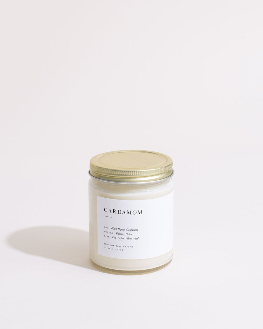 A white jar with a lid, featuring a logo close-up, containing a Cardamom Minimalist Candle.