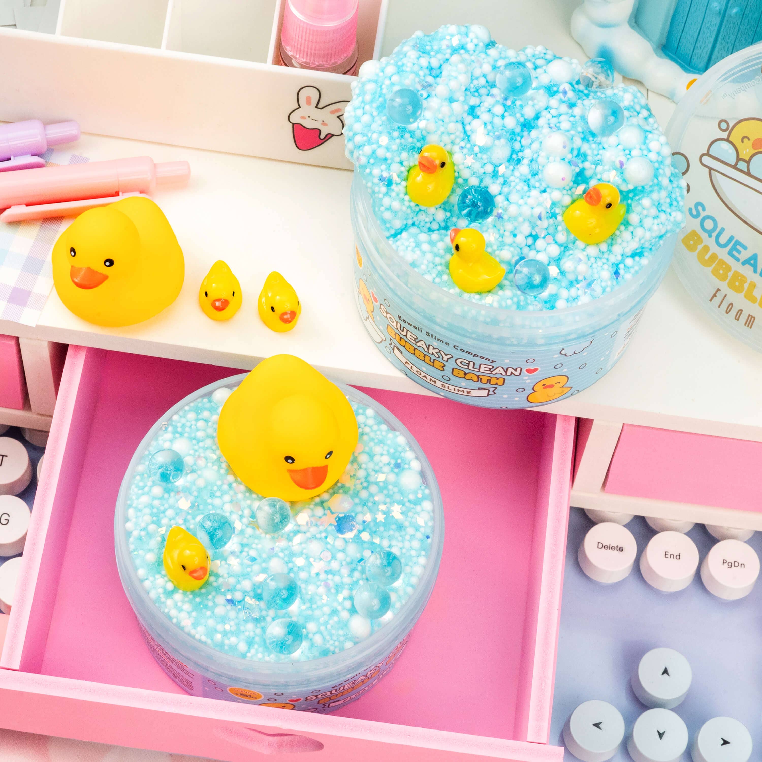 A group of rubber ducks in containers, blue and yellow bubble bath, and a rubber duck in blue water. Squeaky Clean Bubble Bath Floam Slime with sparkly add-ins and a cute squeaky duck toy included.