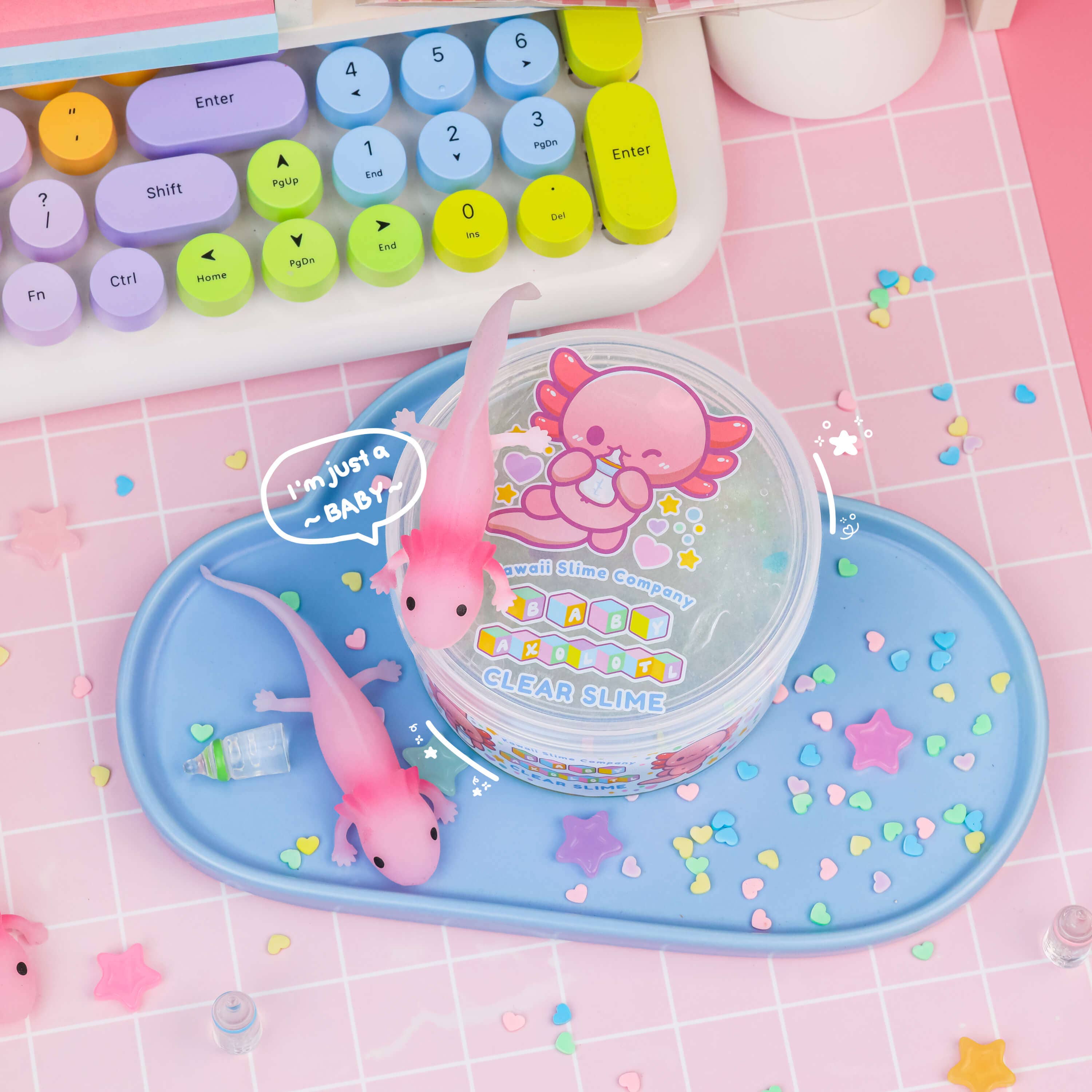 Four clear slime containers with toy lizards, star shapes, and a yellow ball on a blue tray. Perfect pet-like Baby Axolotl Clear Slime set for endless fun.