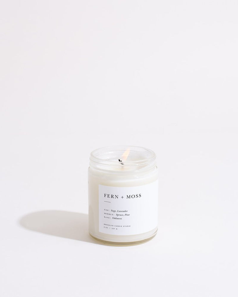 Hand-poured Fern + Moss Minimalist Candle in clear glass jar with modern label, featuring woodsy sage, lavender scents. Made in Brooklyn with soy wax blend.