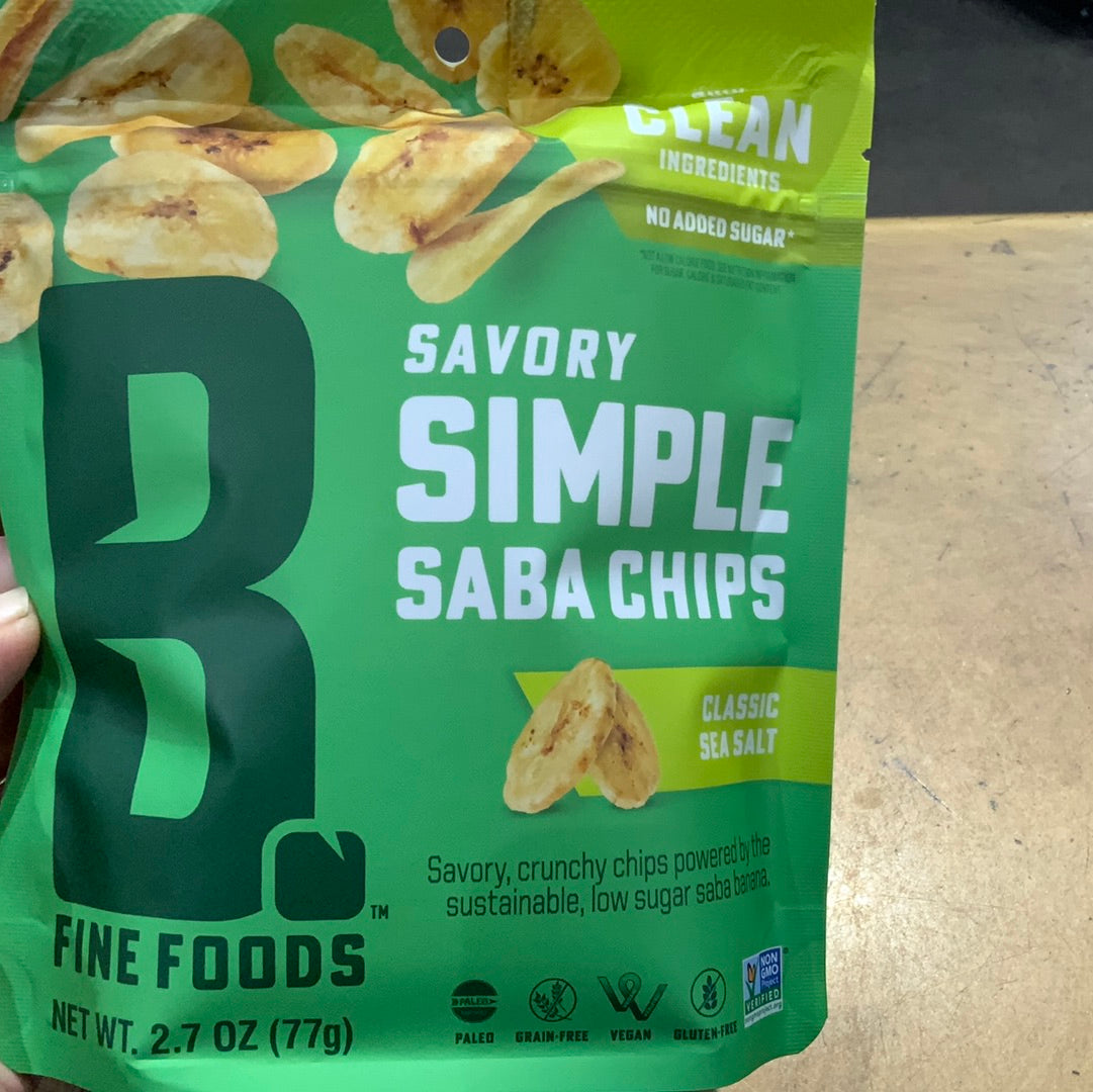 A hand holding a bag of savory saba chips, with green text and a logo on a green surface. Close-up of food.