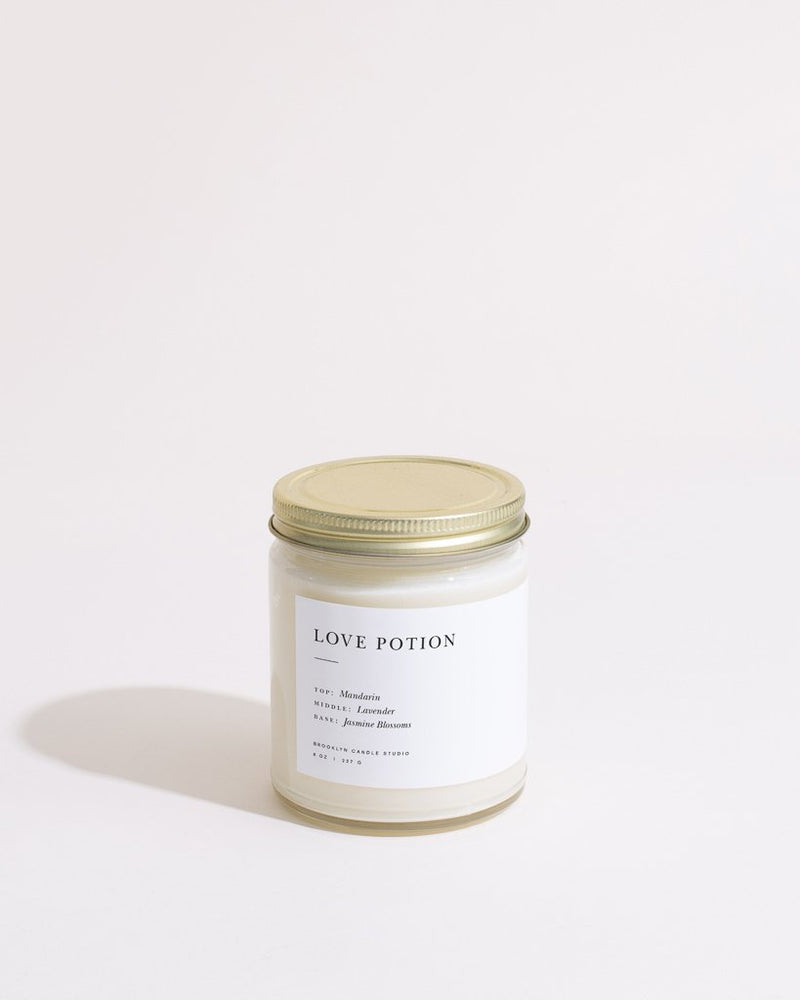 A white candle in a clear glass jar with a gold lid, featuring a modern minimalist label. Fragranced with jasmine, lavender, and mandarin, by Brooklyn Candle Studio.