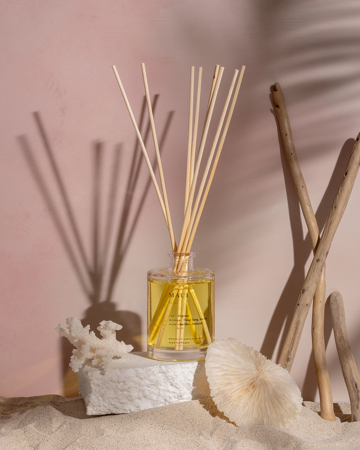 A bottle of Maui Reed Diffuser with wooden sticks on a rock, emitting sea salt, sea moss, driftwood scents. Includes glass bottle, wooden stopper, and 8 rattan reeds.