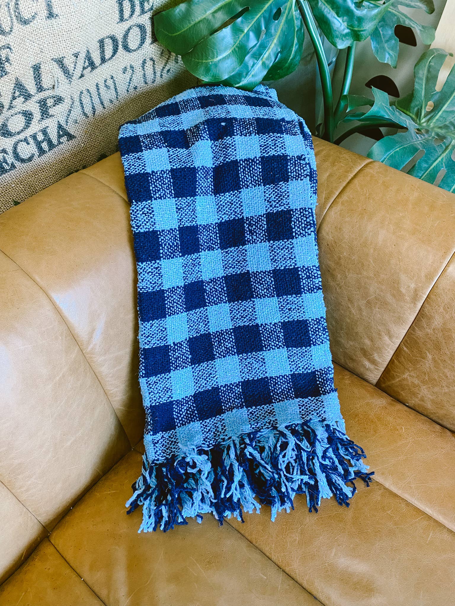 A Heritage Plaid Throw Blanket in navy and light blue checker pattern, draped elegantly on a brown couch, embodying nostalgia and warmth.