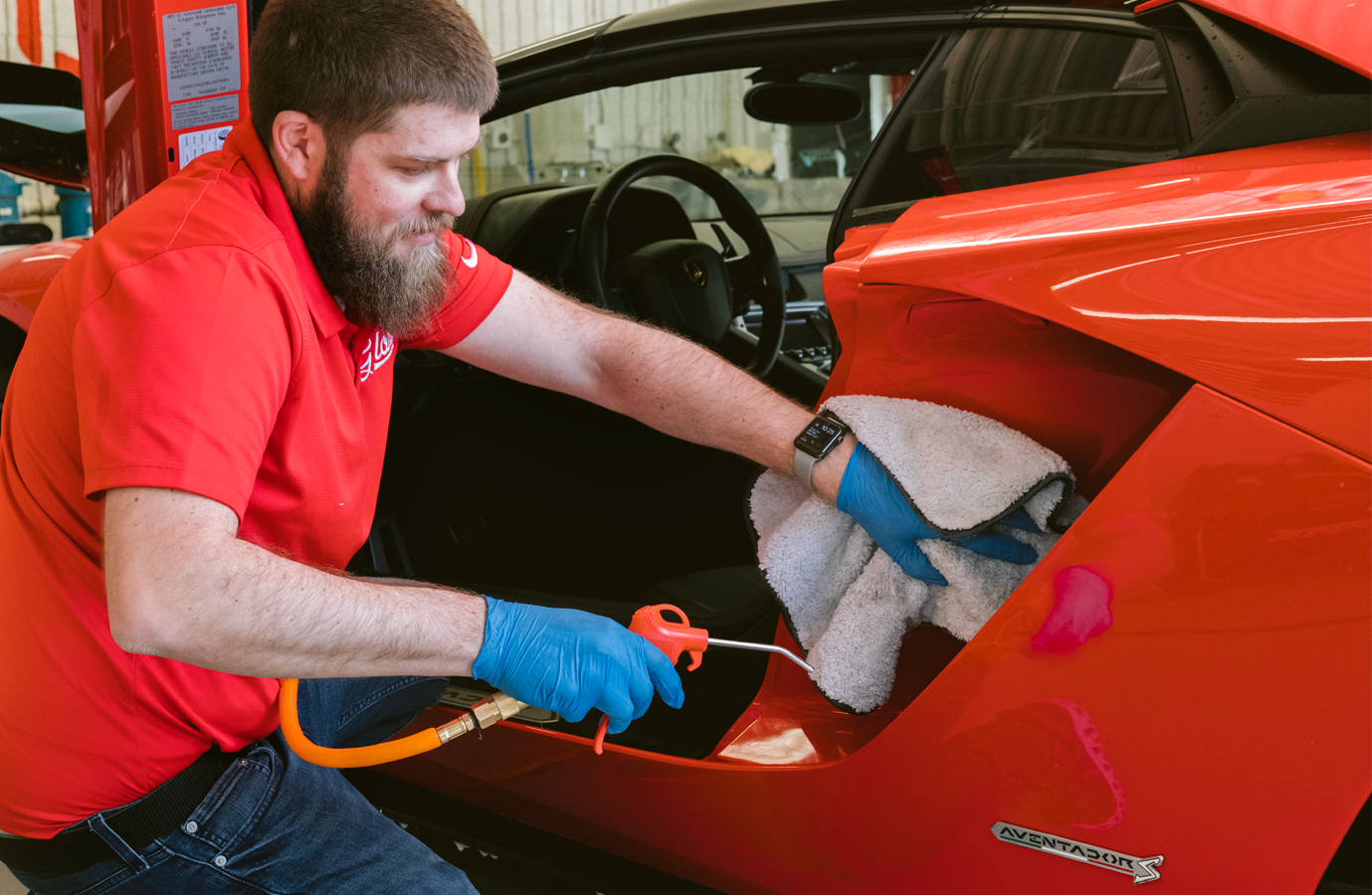 A man detailing a car exterior and interior, showcasing a comprehensive service: Total Interior Detail + Exterior Level 1. Includes hand wash, wheel care, vacuuming, clay bar treatment, and Adam's Polish Ceramic Spray coating for lasting protection.