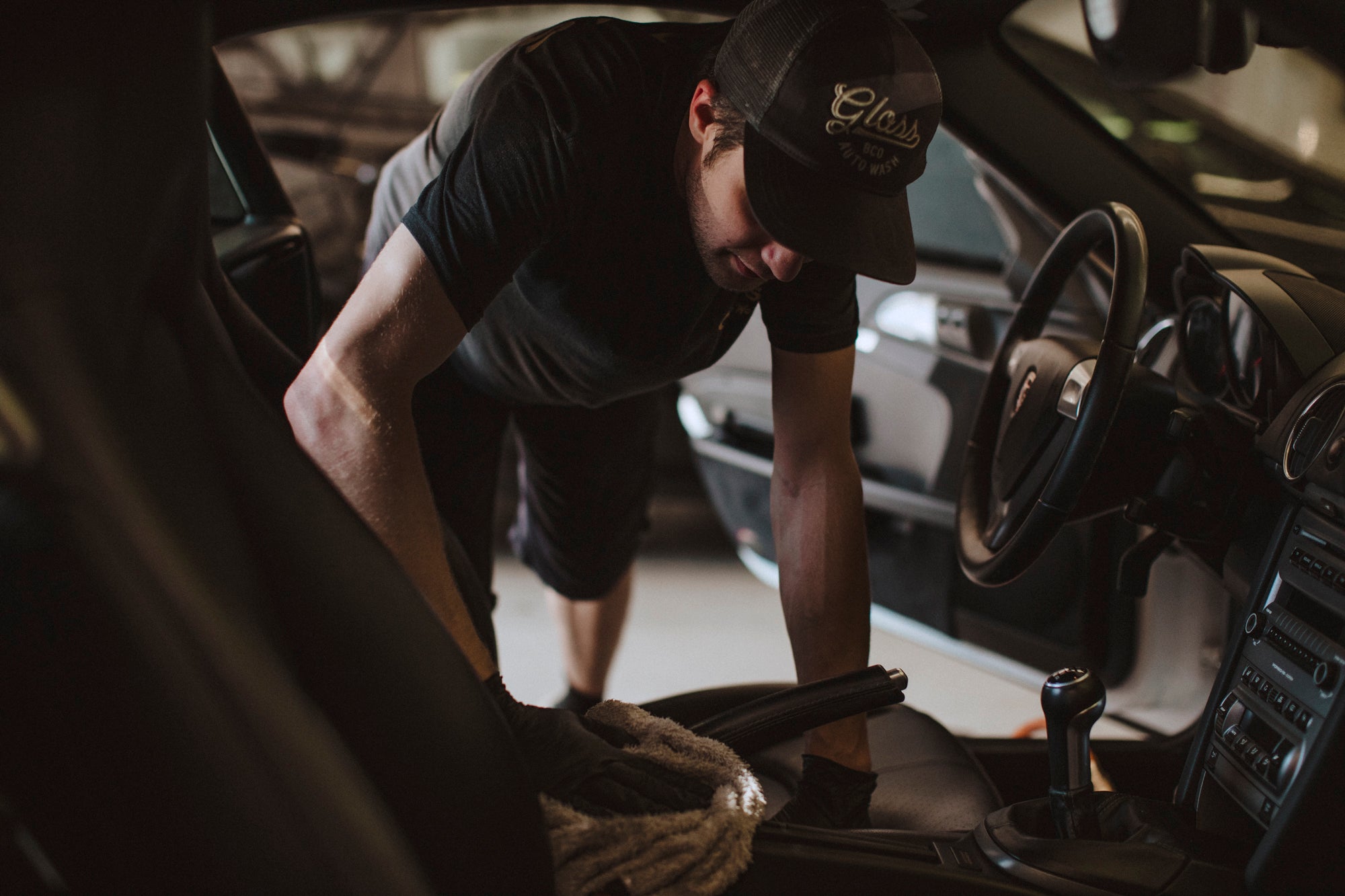 A man cleaning a car's interior, focusing on dash, console, and seats. Touch Up Detail service includes vacuuming, wiping down leather seats, and deep cleaning for a refreshed vehicle interior.