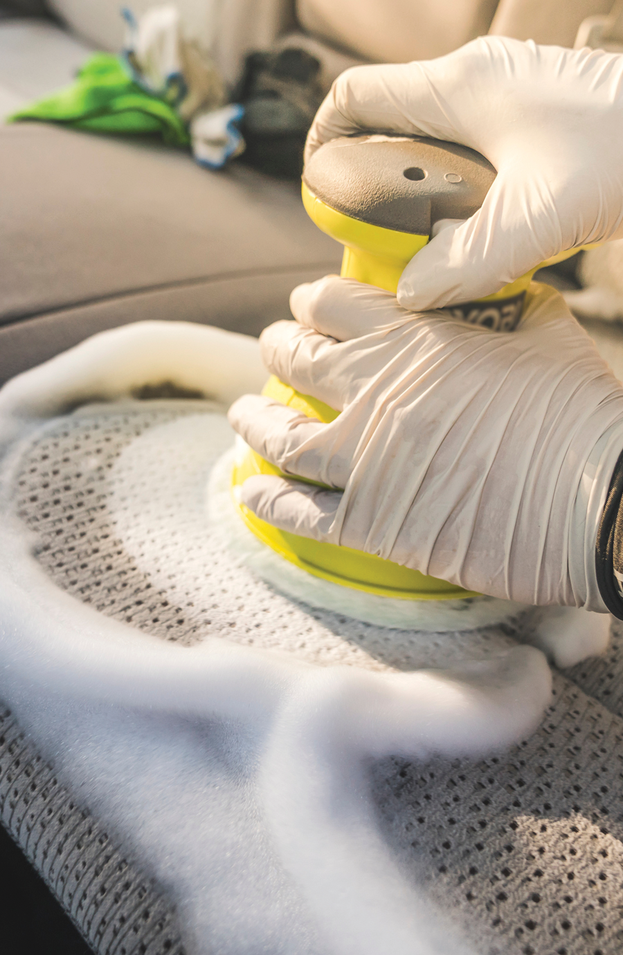 Person using Seat Shampoo & Extraction service: steam extraction for deep cleaning car seat crevices, removing stains and debris effectively.