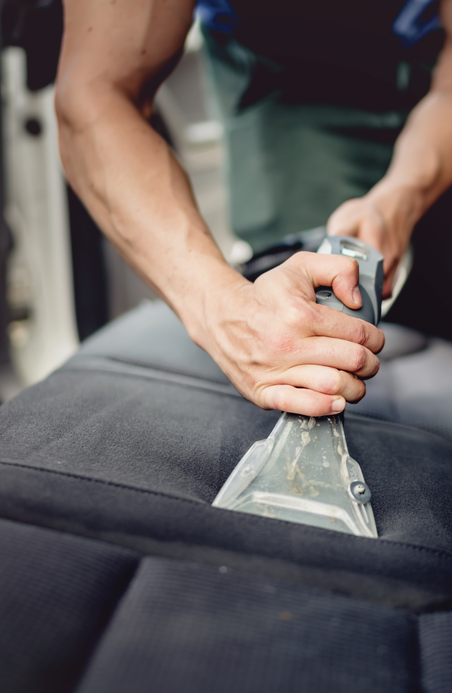 A person using a vacuum cleaner for Seat Shampoo & Extraction service, removing debris and dirt from car seats. Includes steam extraction and stain removal.