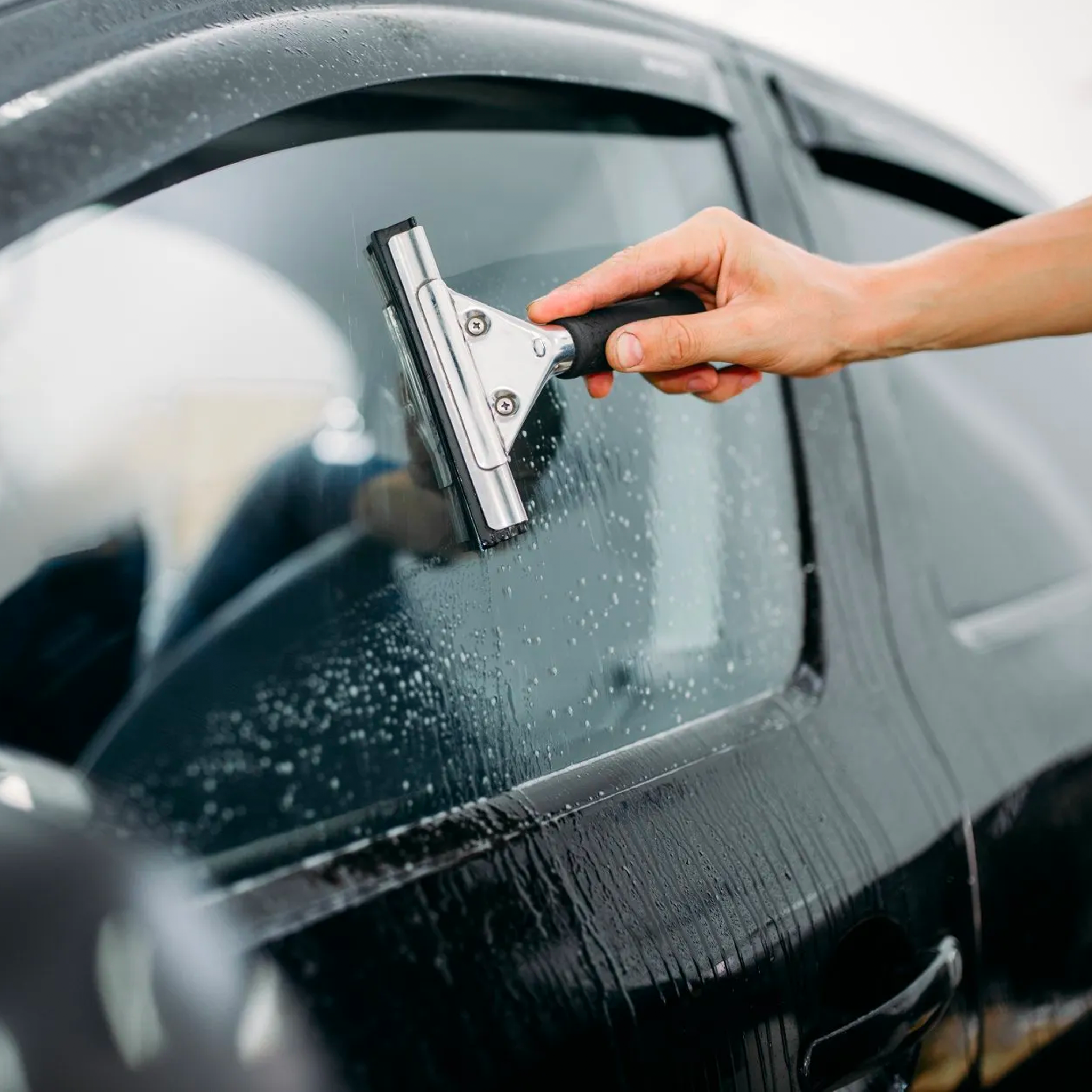 A person uses a squeegee to apply Front Window Match Tint on a car window. XPEL brand tint films offer privacy, heat reduction, and style customization. Prices vary based on car type and film choice.