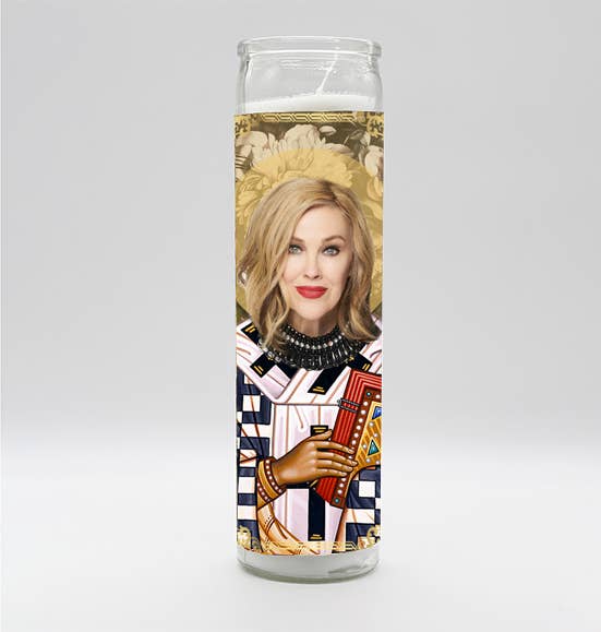A tall white unscented candle featuring a parody art design of Saint Moira Rose, hand-poured in Mexico and assembled in the USA.