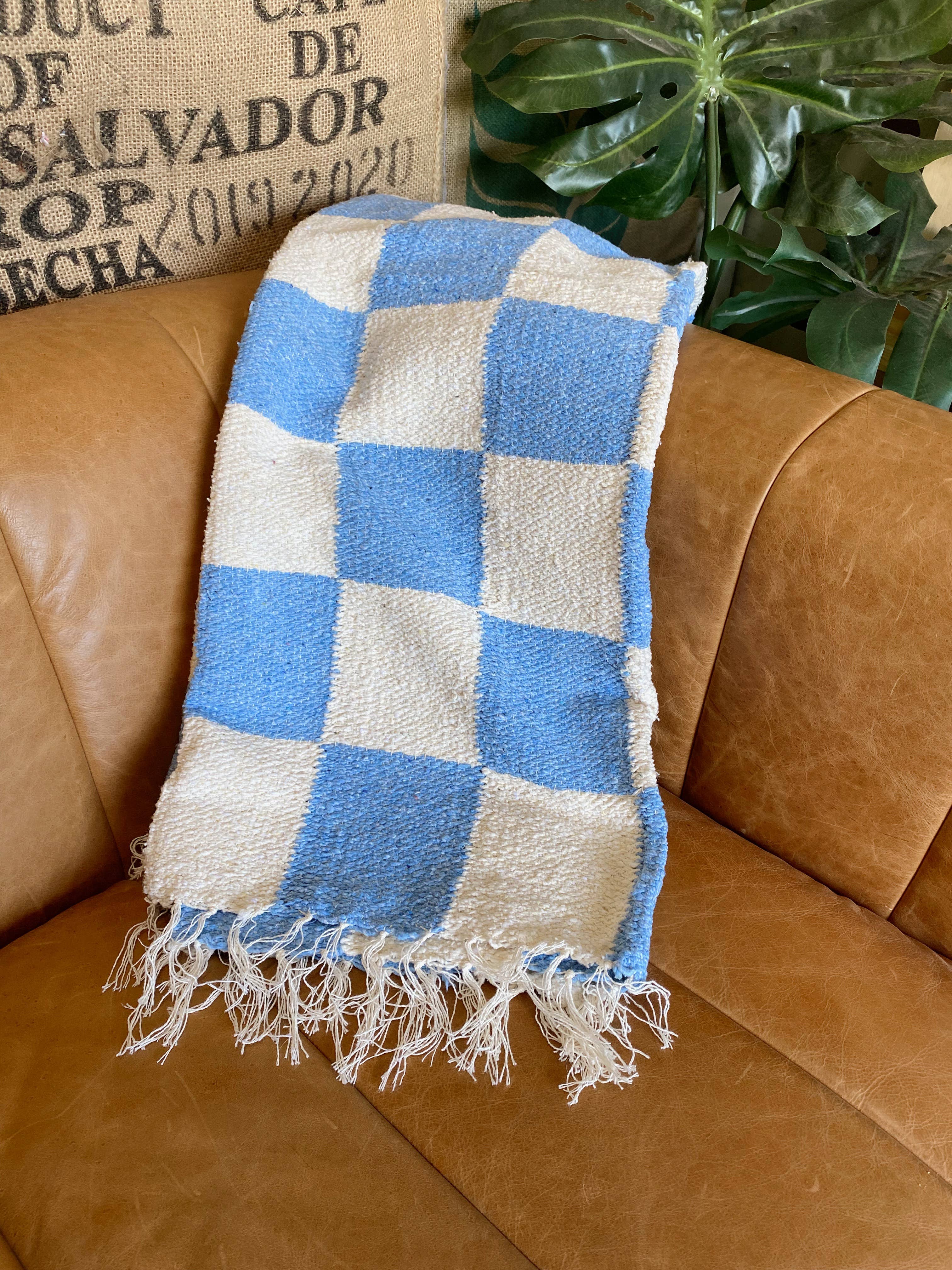 Handmade heavyweight Laguna Checker Throw on brown couch, green plant nearby. Sustainable blend of cotton, acrylic, polyester. Versatile as rug. Measures 83 x 52 inches. Crafted in California, made in Mexico.