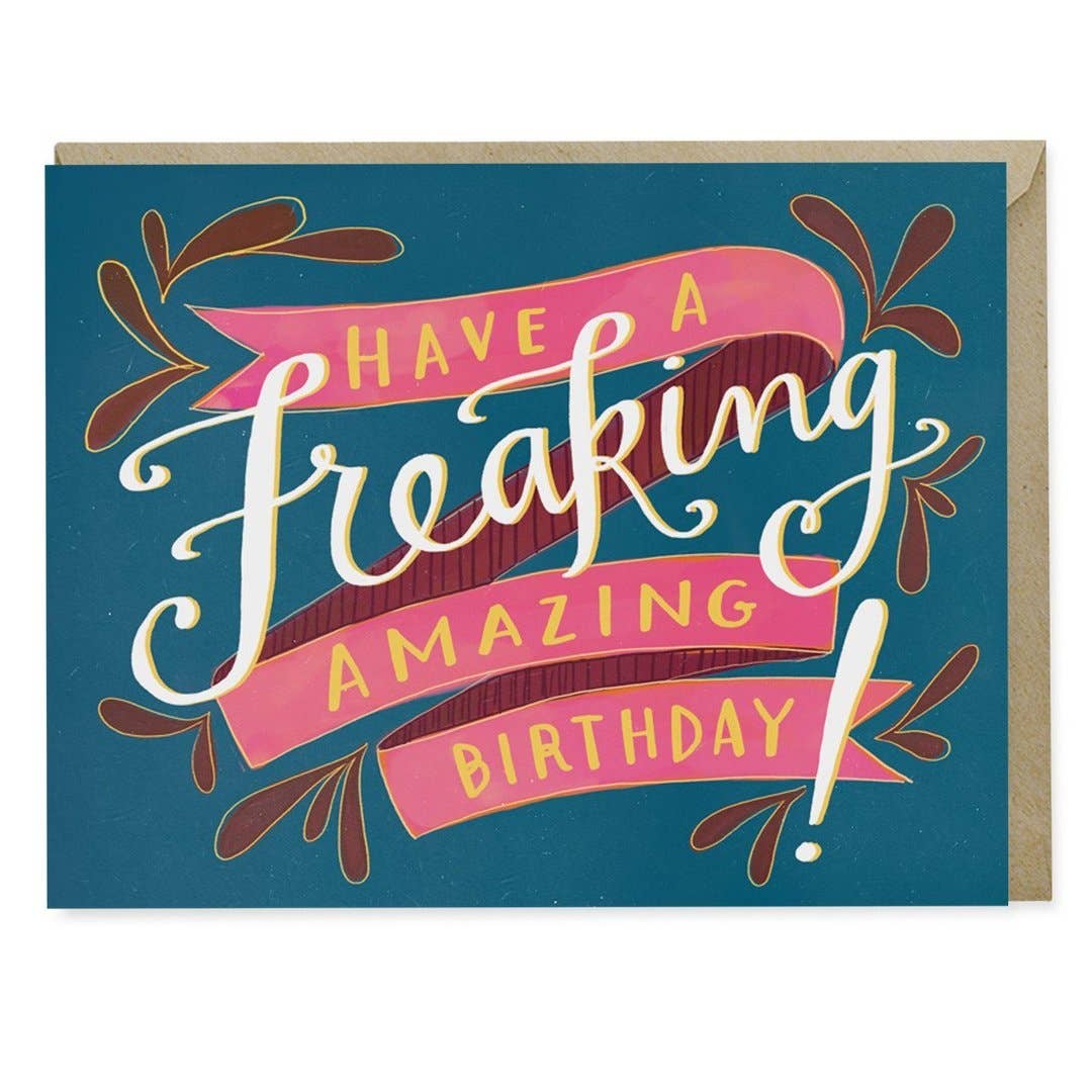 A close-up of the Freaking Amazing Birthday Card, featuring white text on a blue and pink design. Blank inside, A2 size, USA printed on matte stock, with a kraft envelope.