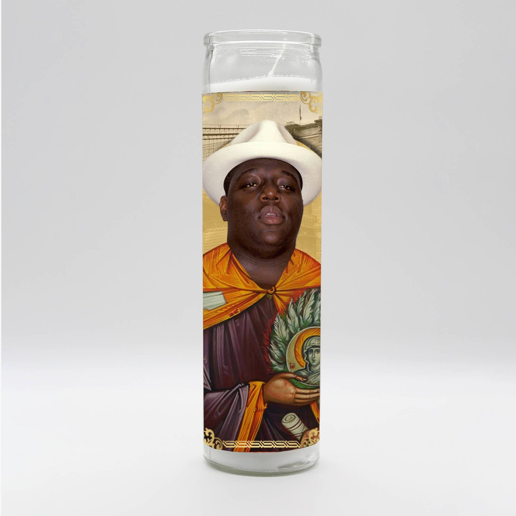A man in a white hat holds The Notorious B.I.G. Candle, hand-poured in Mexico, with a close-up of a painting in the background.