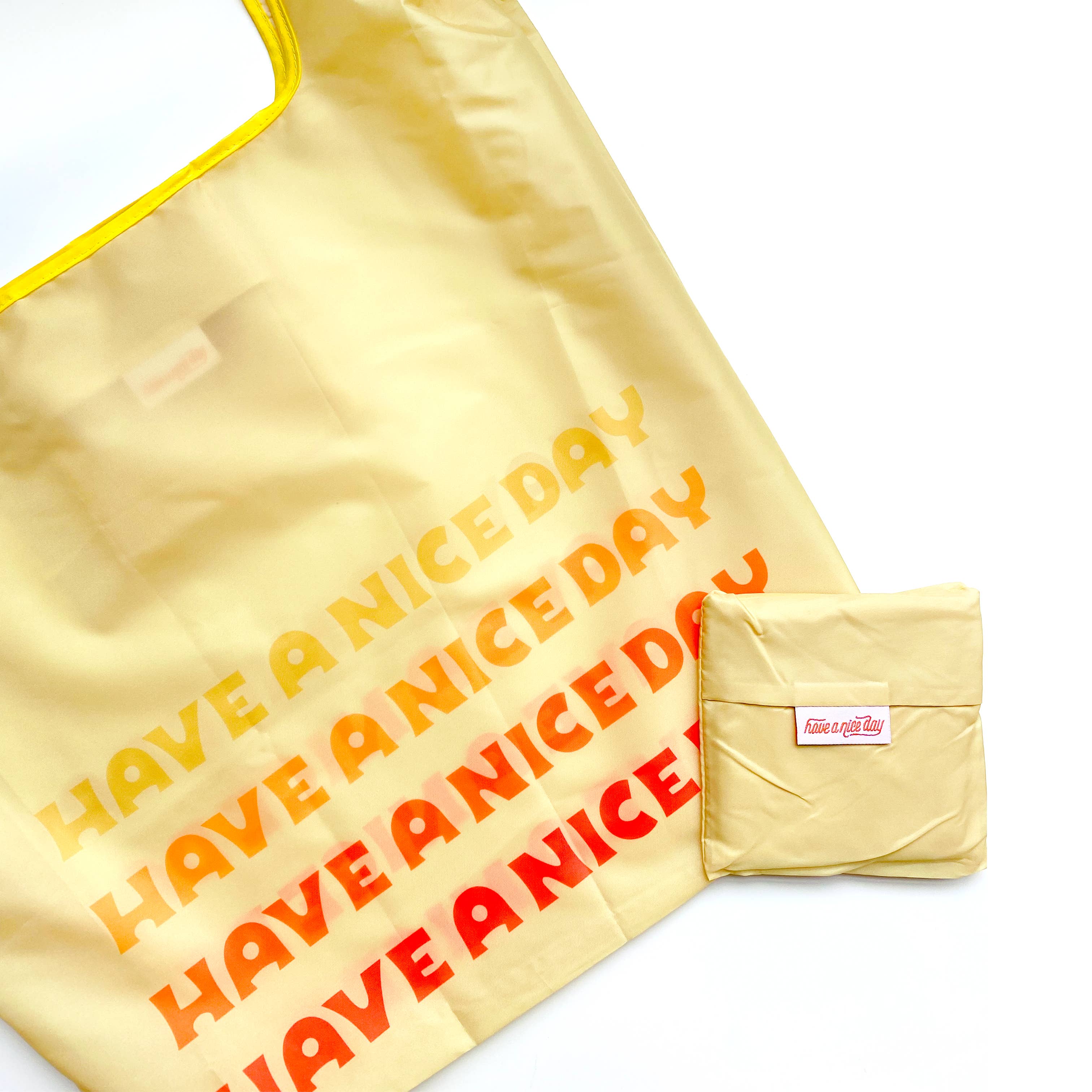 A yellow Desert Days reusable nylon bag with red text, folded, showcasing a small wallet. Made of 100% nylon, folds into pocket, 25 x 14 x 5.