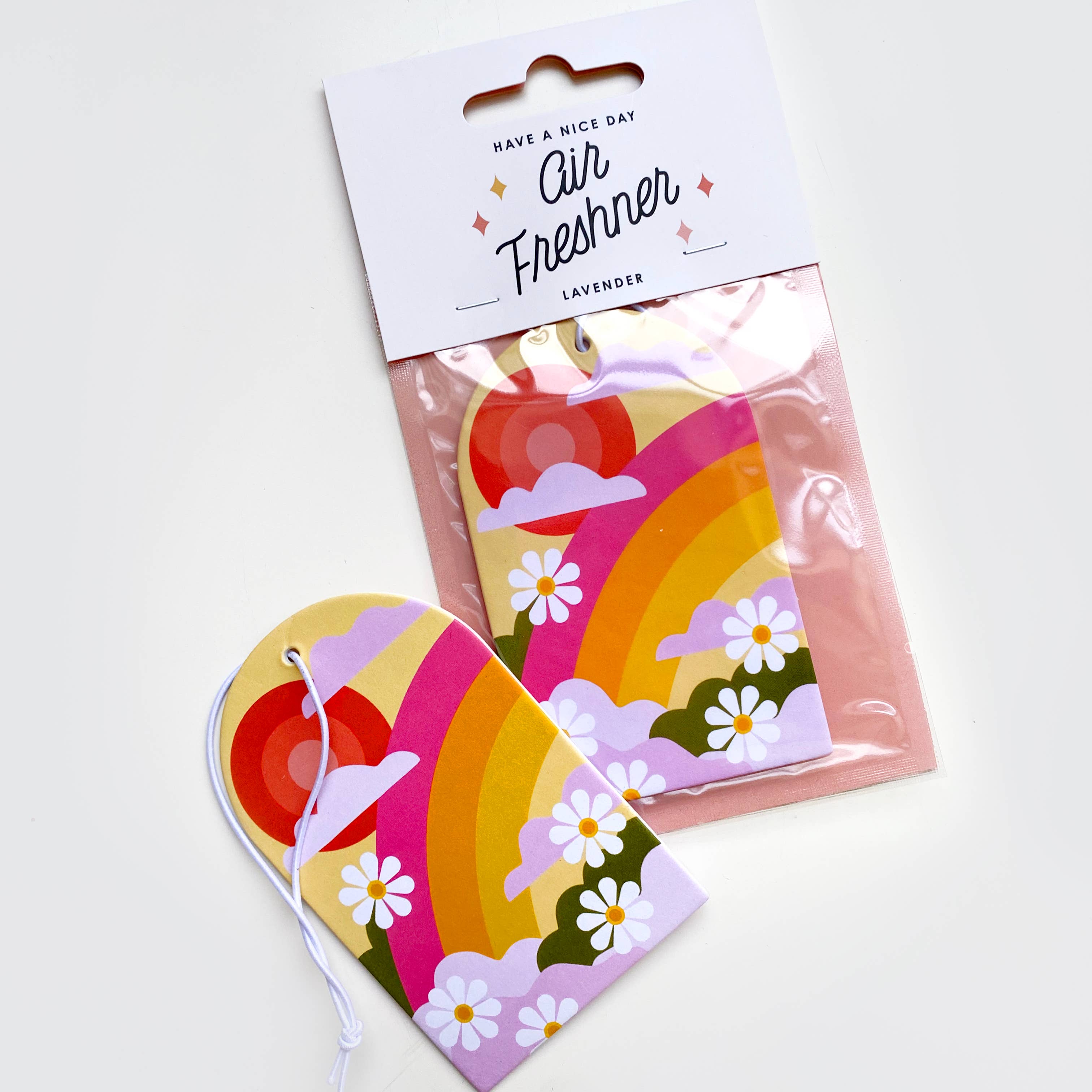 A lavender-scented air freshener named Along For The Ride, showcasing a colorful package with floral and rainbow tags. Dimensions: 2.5in x 4.1in.