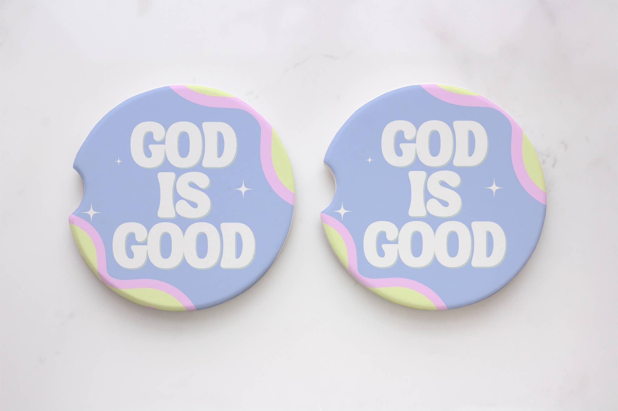 Two round car coasters with God Is Good text, one blue and pink circle, and a white star on blue background. Absorbent neoprene material with durable print. Packaged on a car coasters card. Size: 2.6 x 0.125.