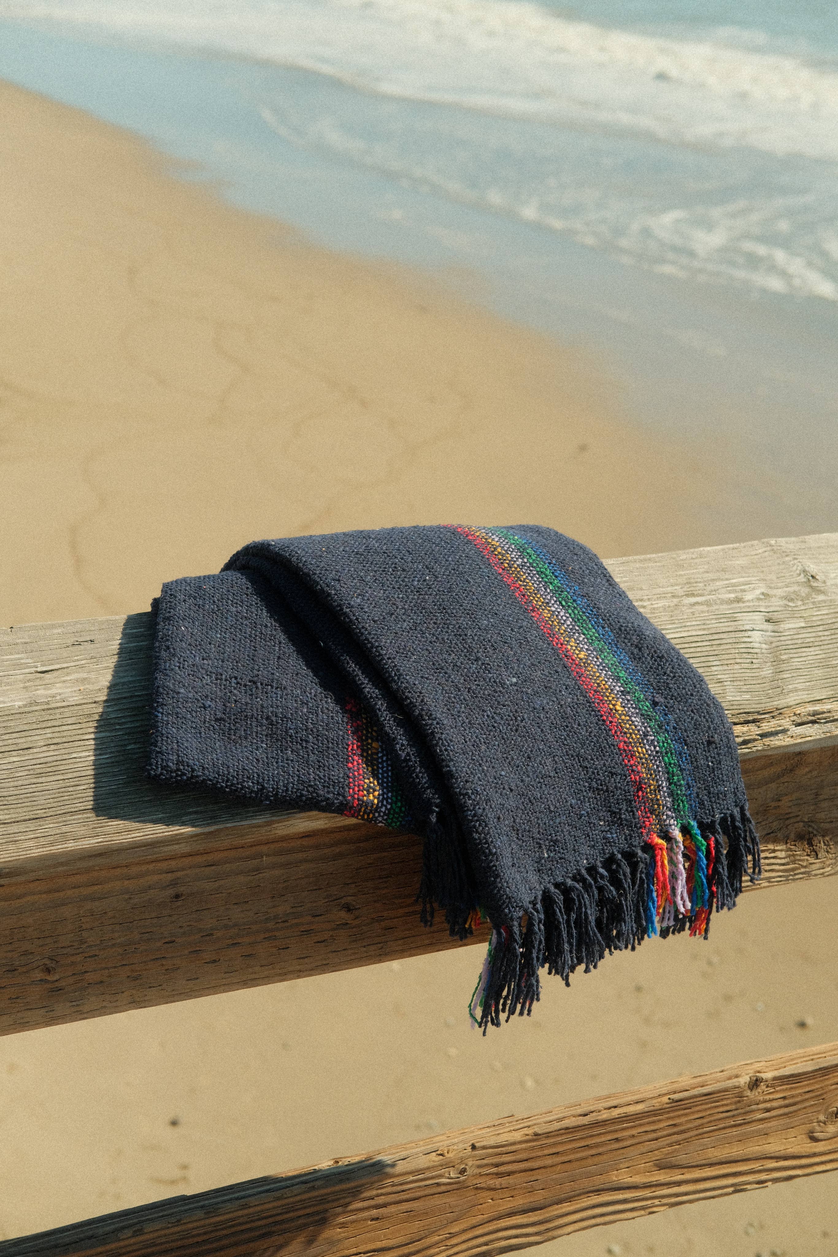 A sustainable Retro Rainbow Navy throw blanket, made from reclaimed fibers, ideal for home or outdoor use. Measures 73 x 48. Crafted in Mexico.