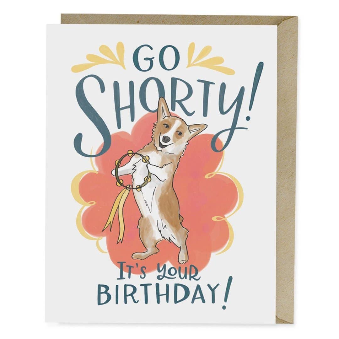 A birthday card featuring a dog holding a ribbon and playing a tambourine, inspired by studio corgi George. A2 size, blank inside, printed on matte stock, with a kraft envelope.