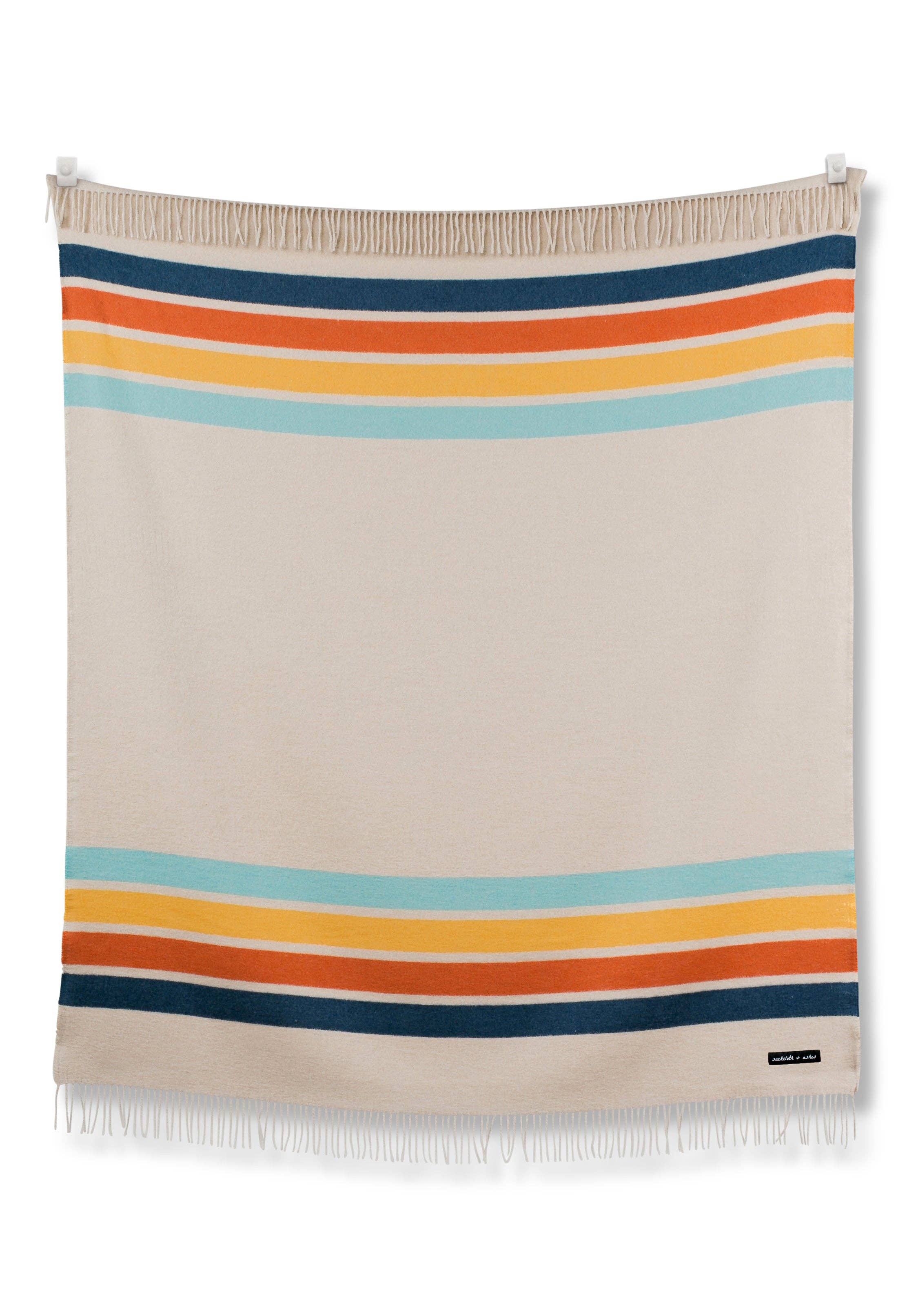 Vintage-inspired Camp Coast blanket made from recycled materials, featuring multicolored stripes. Measures 70”l x 60”w, crafted for comfort and durability. Ideal for outdoor escapes.