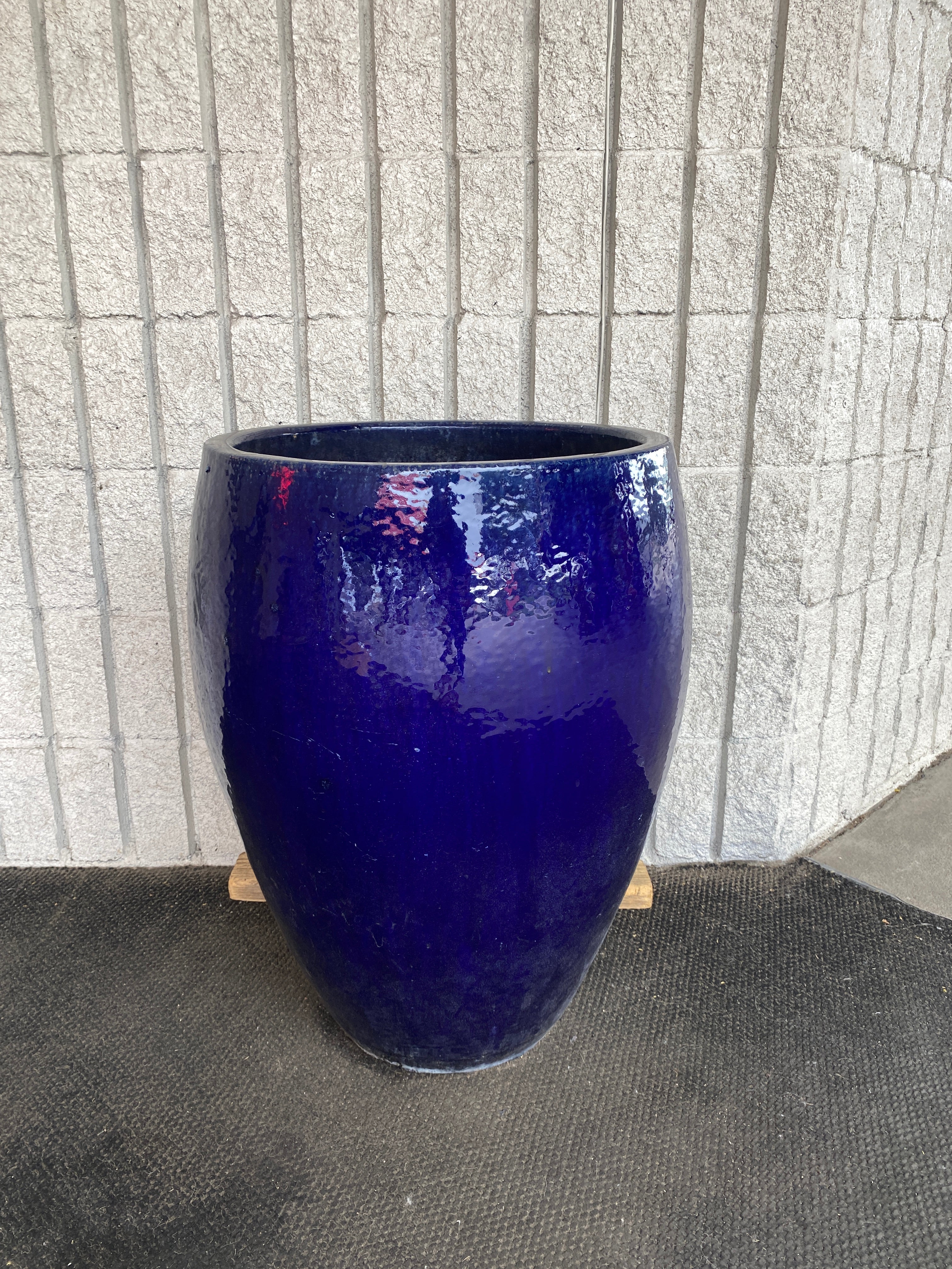 A blue vase with red flowers on a wooden stand, reflecting a person, fitting the Old Puddle Planter style.