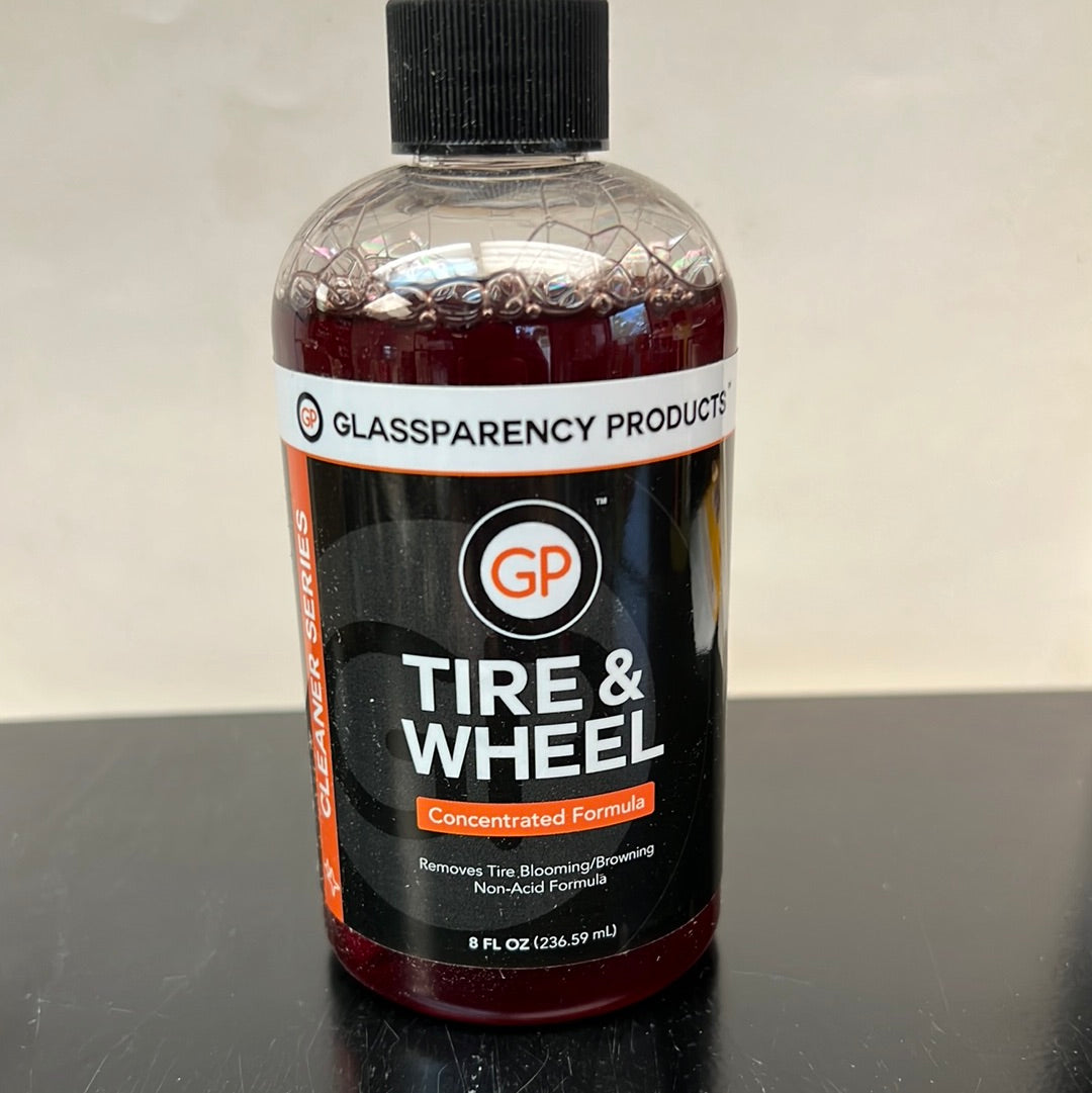 A close-up of GP Tire & Wheel liquid solution in a glass bottle with a logo and label visible.