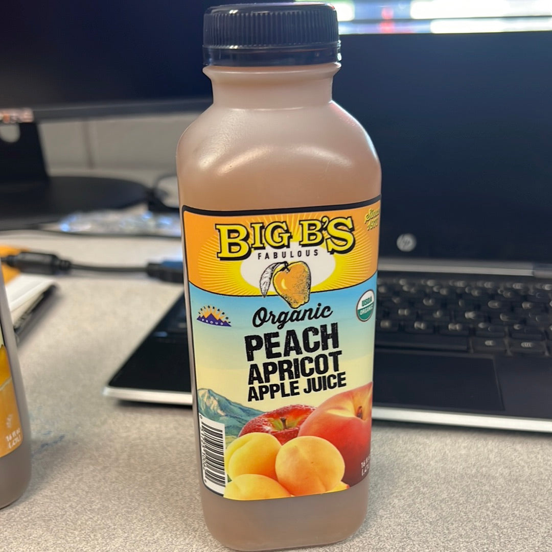 A bottle of Big B’s peach apricot juice, featuring a label and fruit close-ups, on a desk.